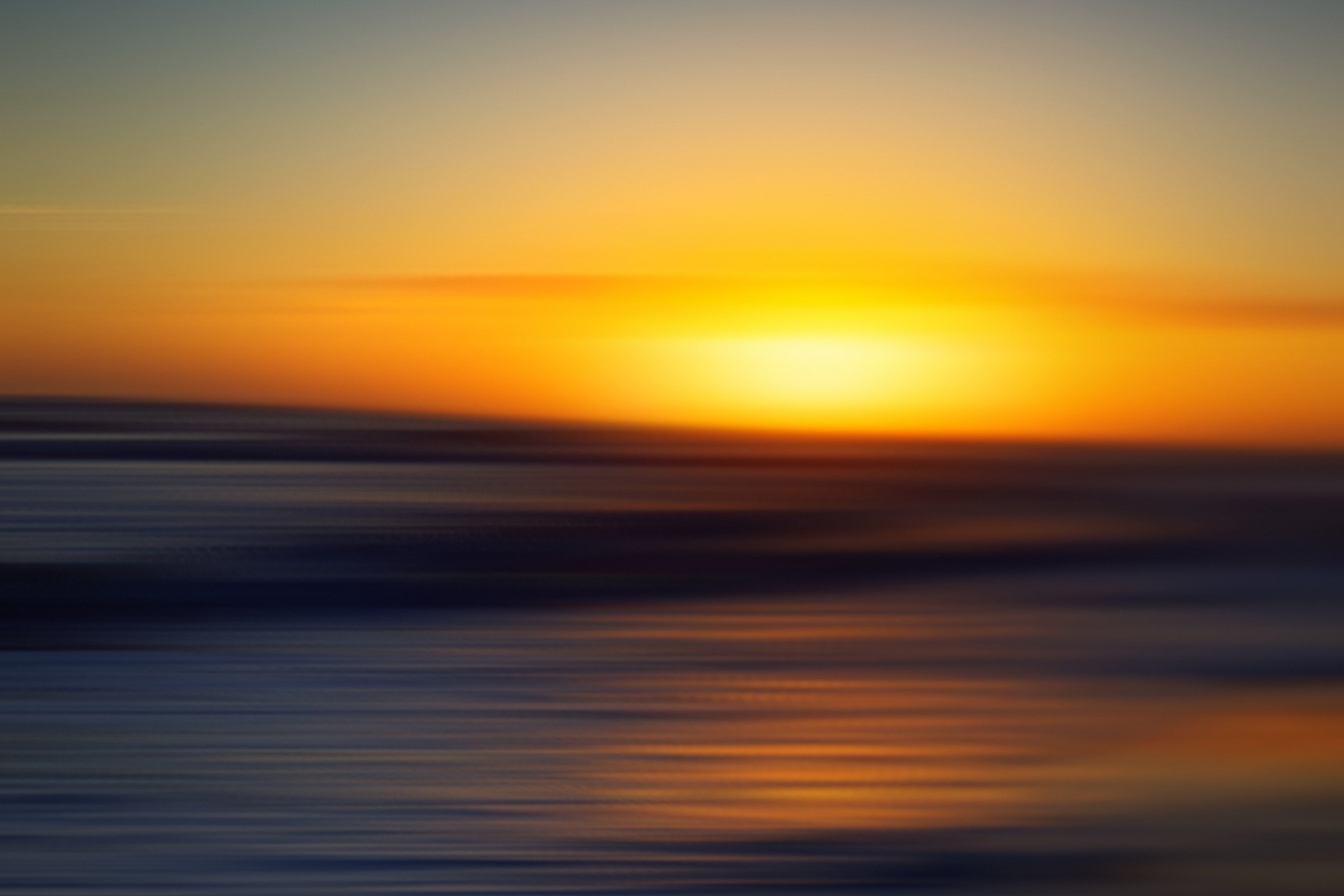 Horizontal streaks of gold sun and orange sky over dark water.