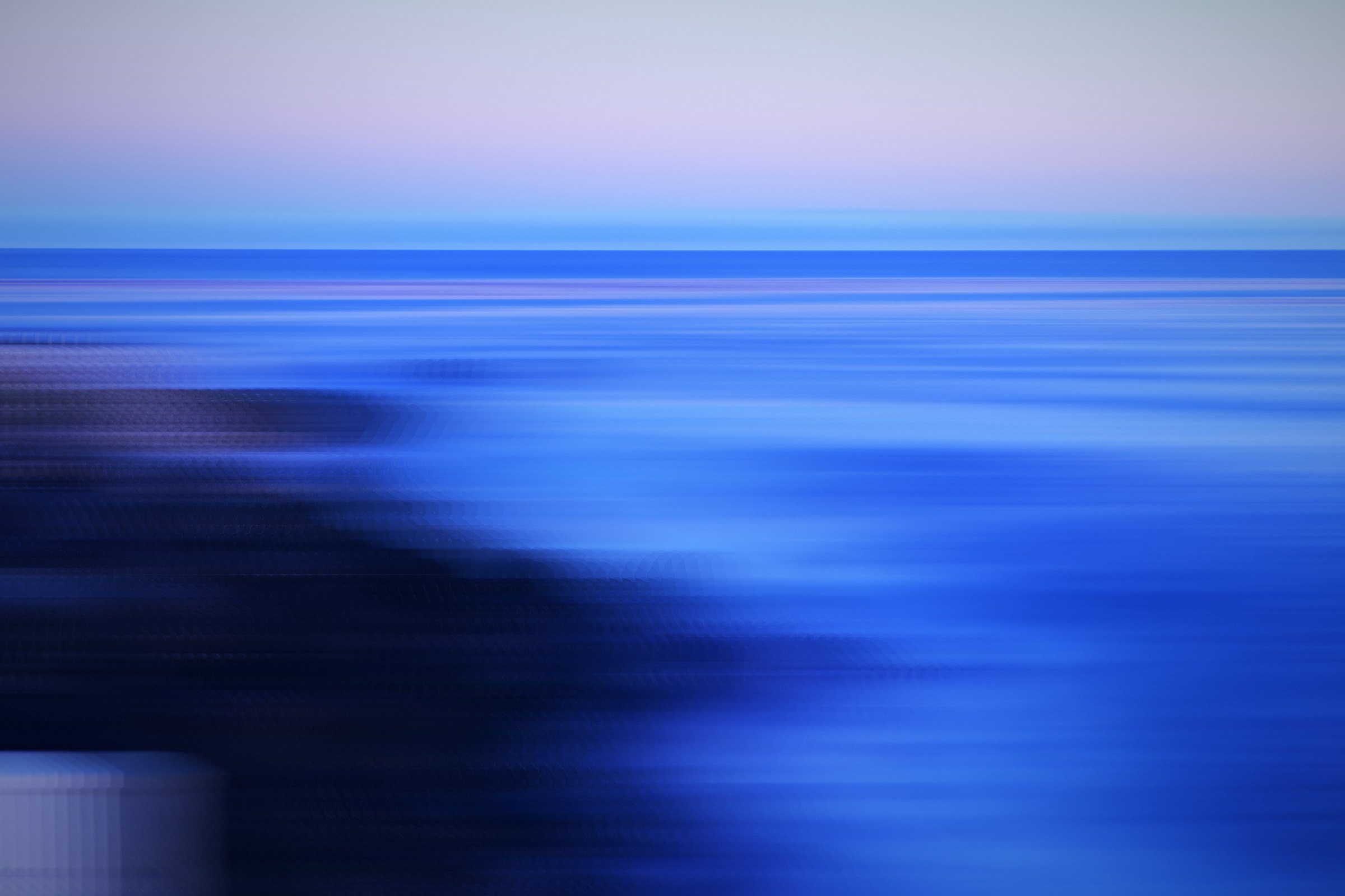 Streaks of deep blue sea and dark rock under a pale sky.
