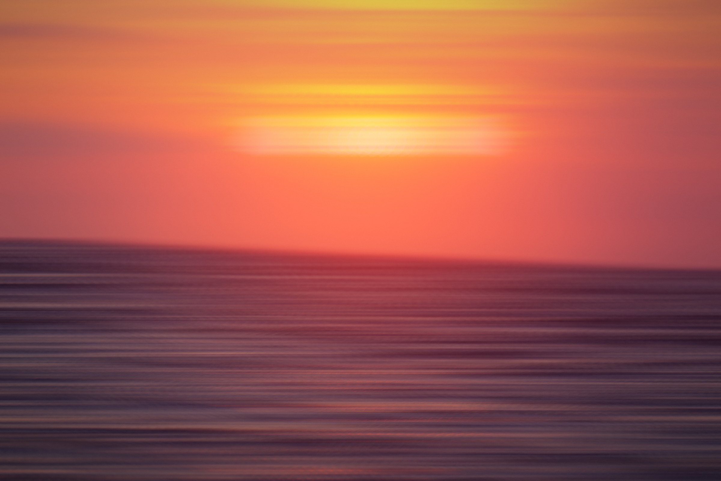 Coral-red sunset band over horizontal streaks of dark sea.