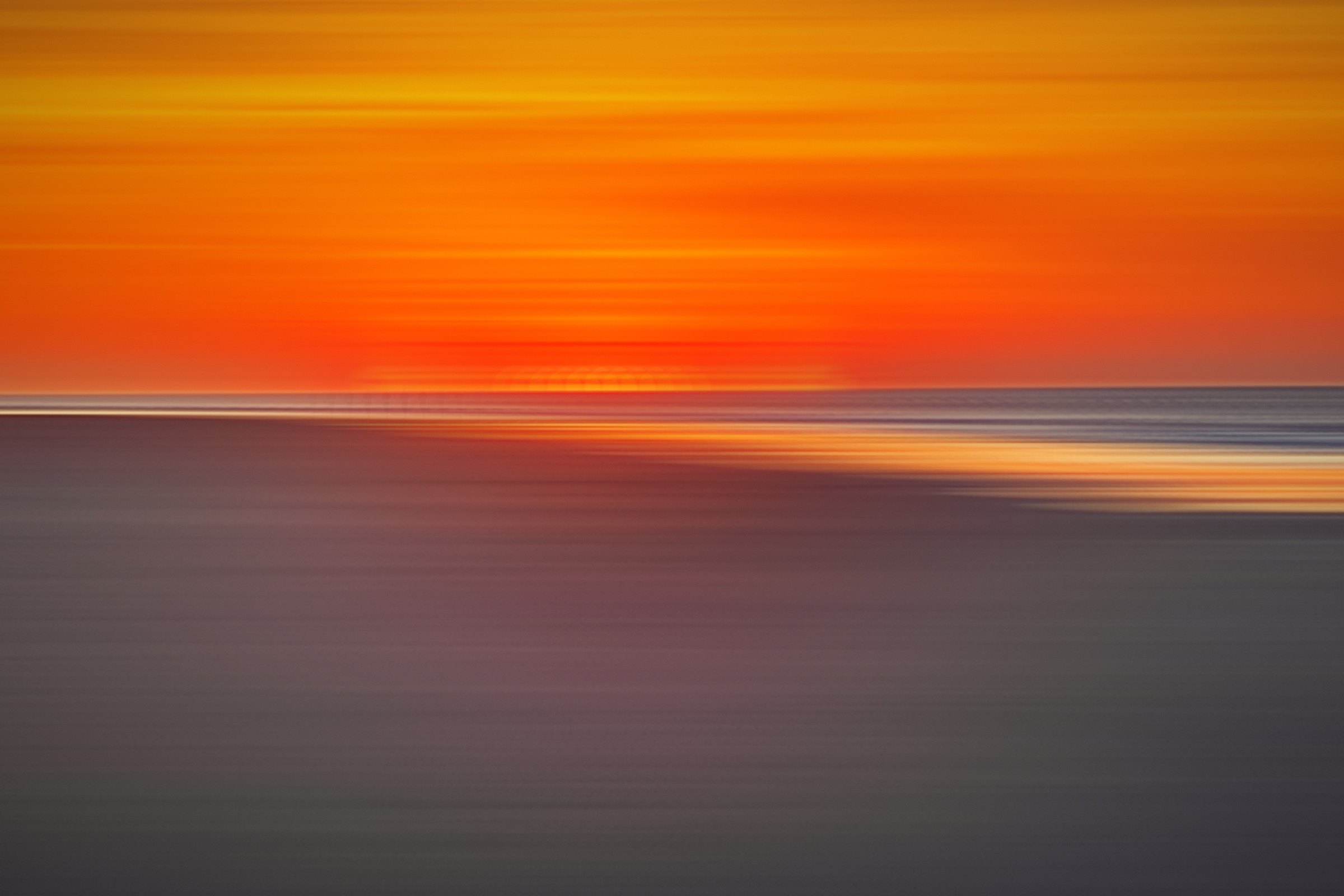 Orange and red sky streaked over dark sand.