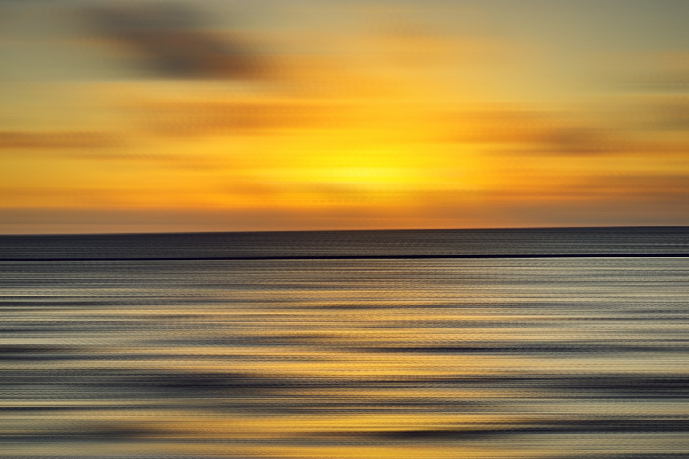 Gold sun band over streaks of blue sea at dawn.
