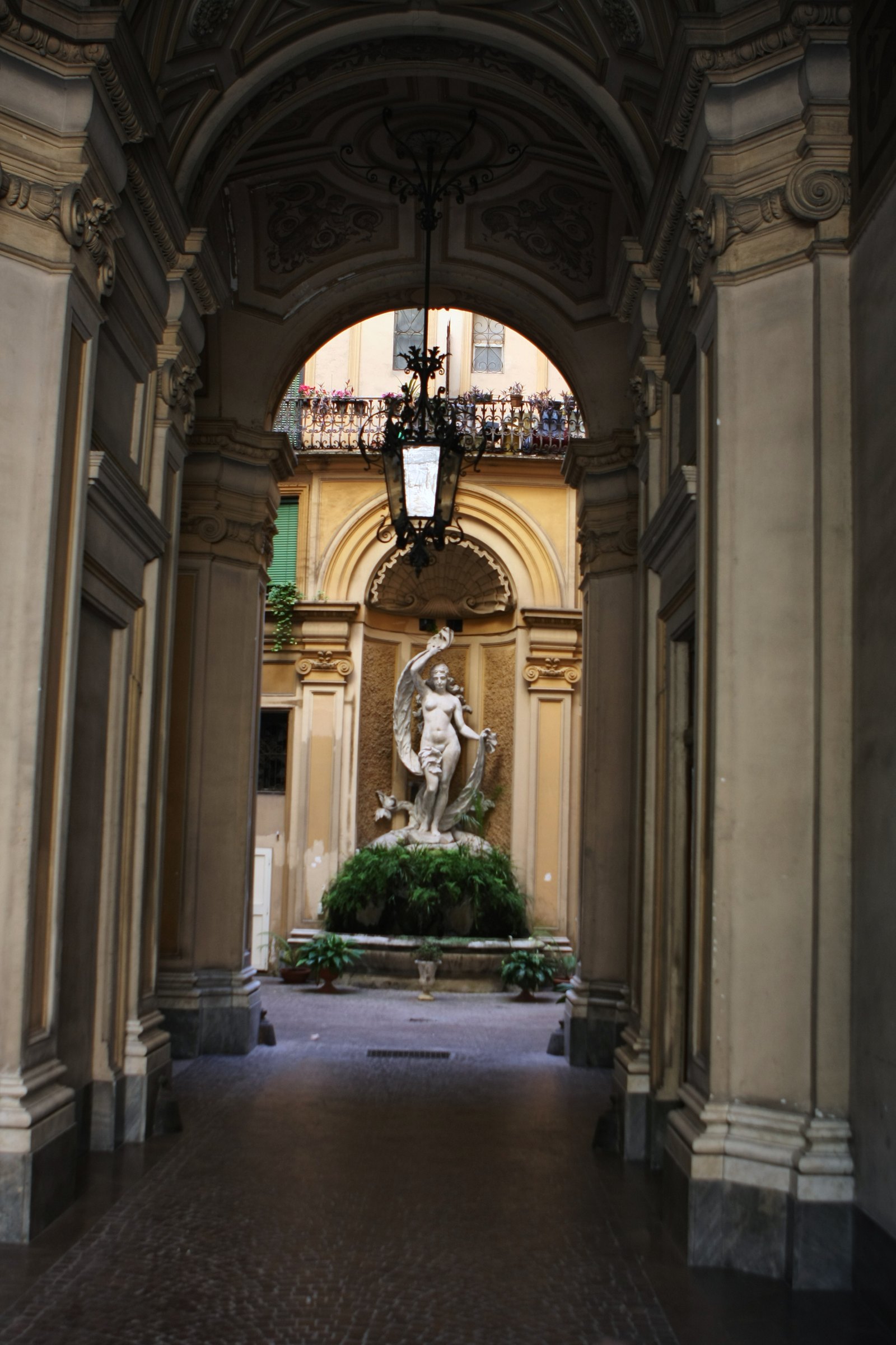 A long arcade leading to a statue in a courtyard niche.