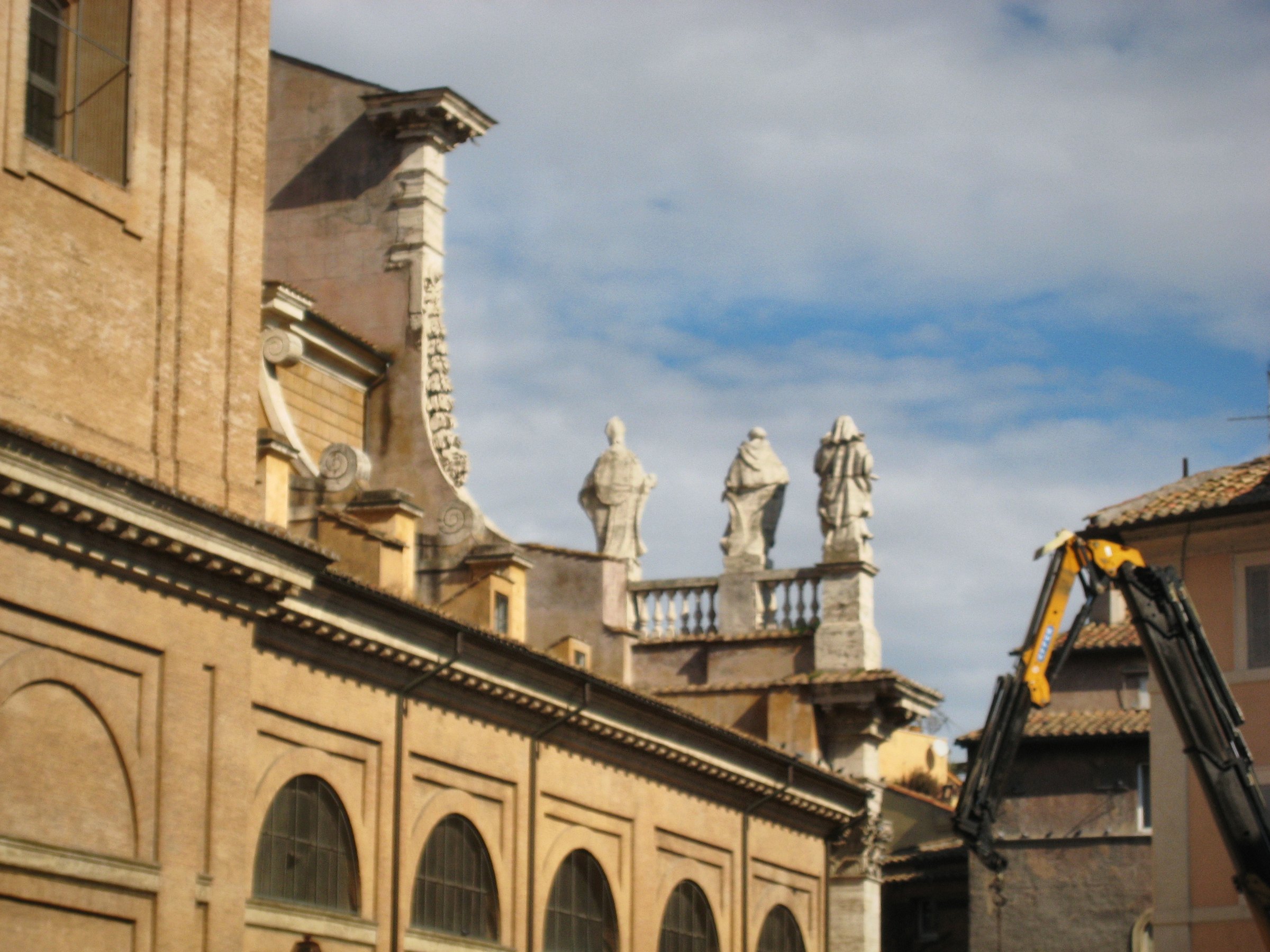 A row of statues along a building's roofline against cloud.