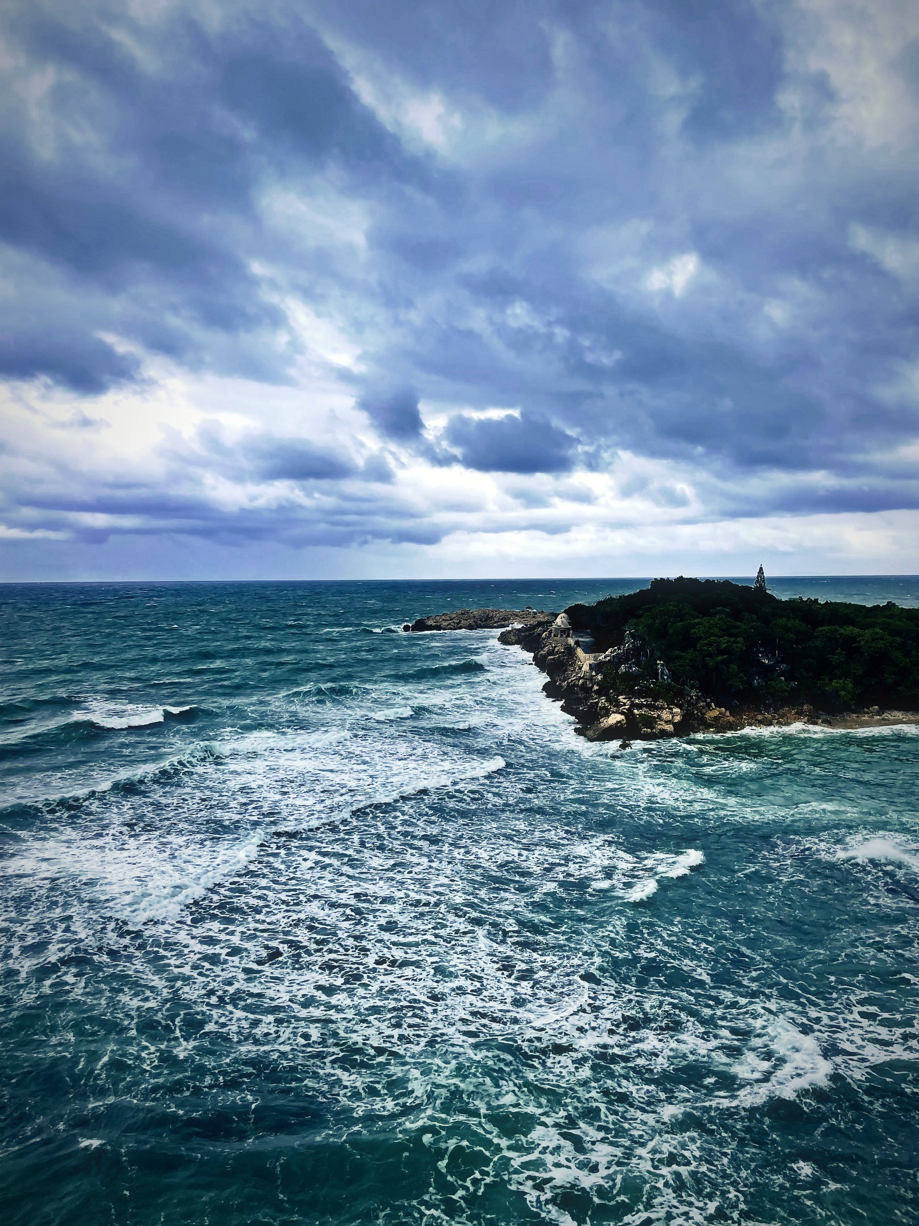 Rough teal surf churning below a dark headland under heavy storm clouds.