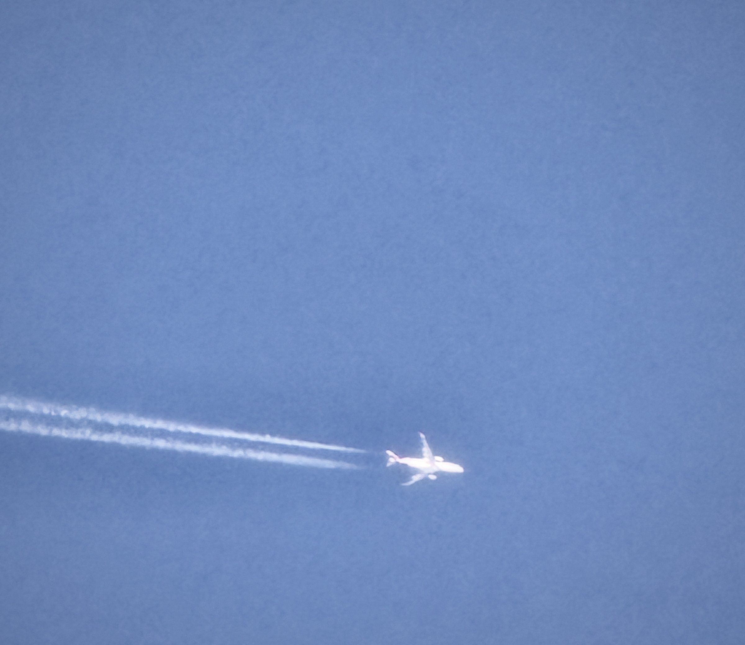 A jet trailing a long white contrail across a deep blue sky.