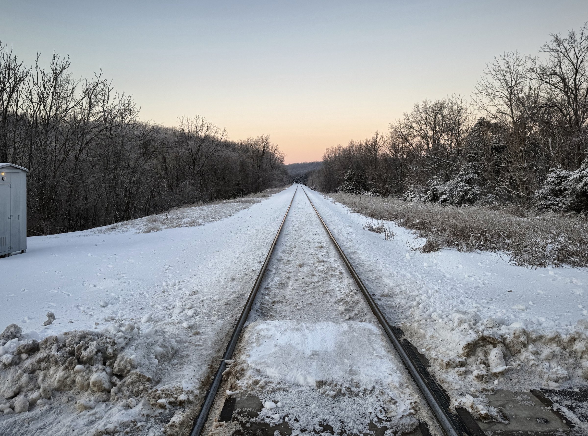 Railroad tracks running straight through fresh snow toward bare winter trees.