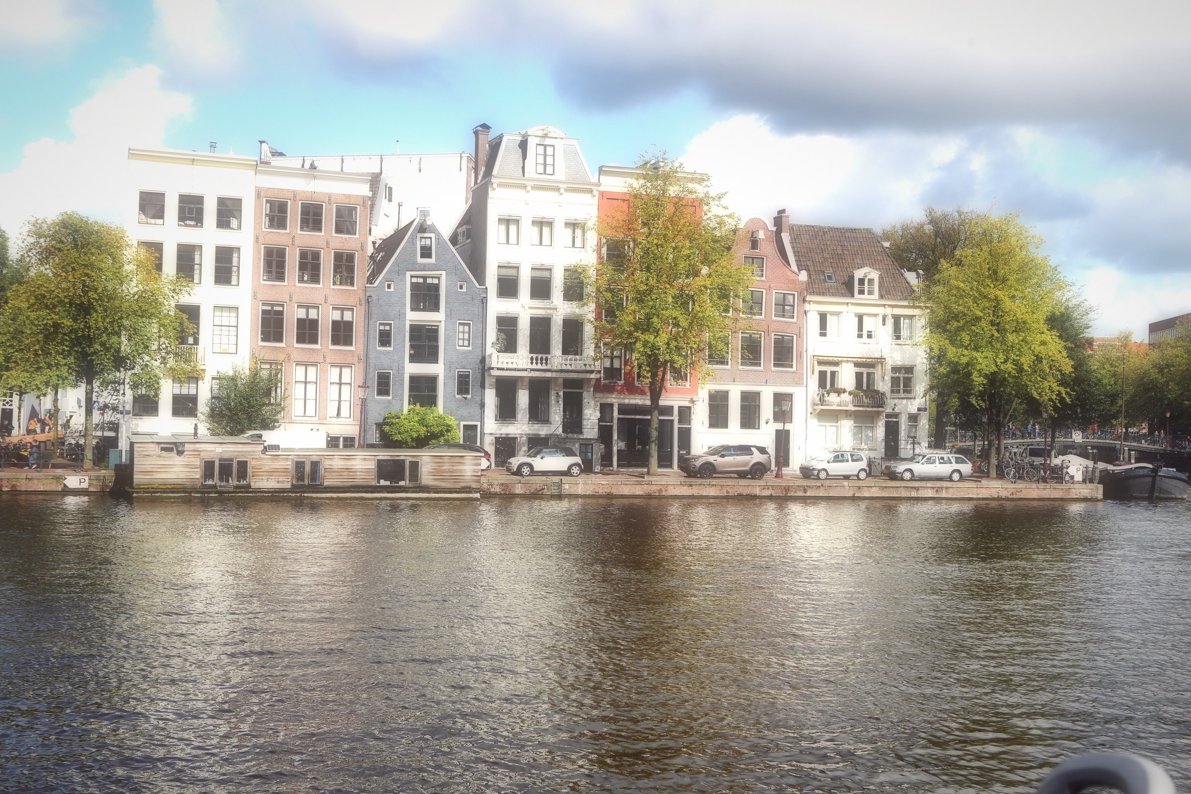 A row of pale canal houses beside a wide river under soft cloud.