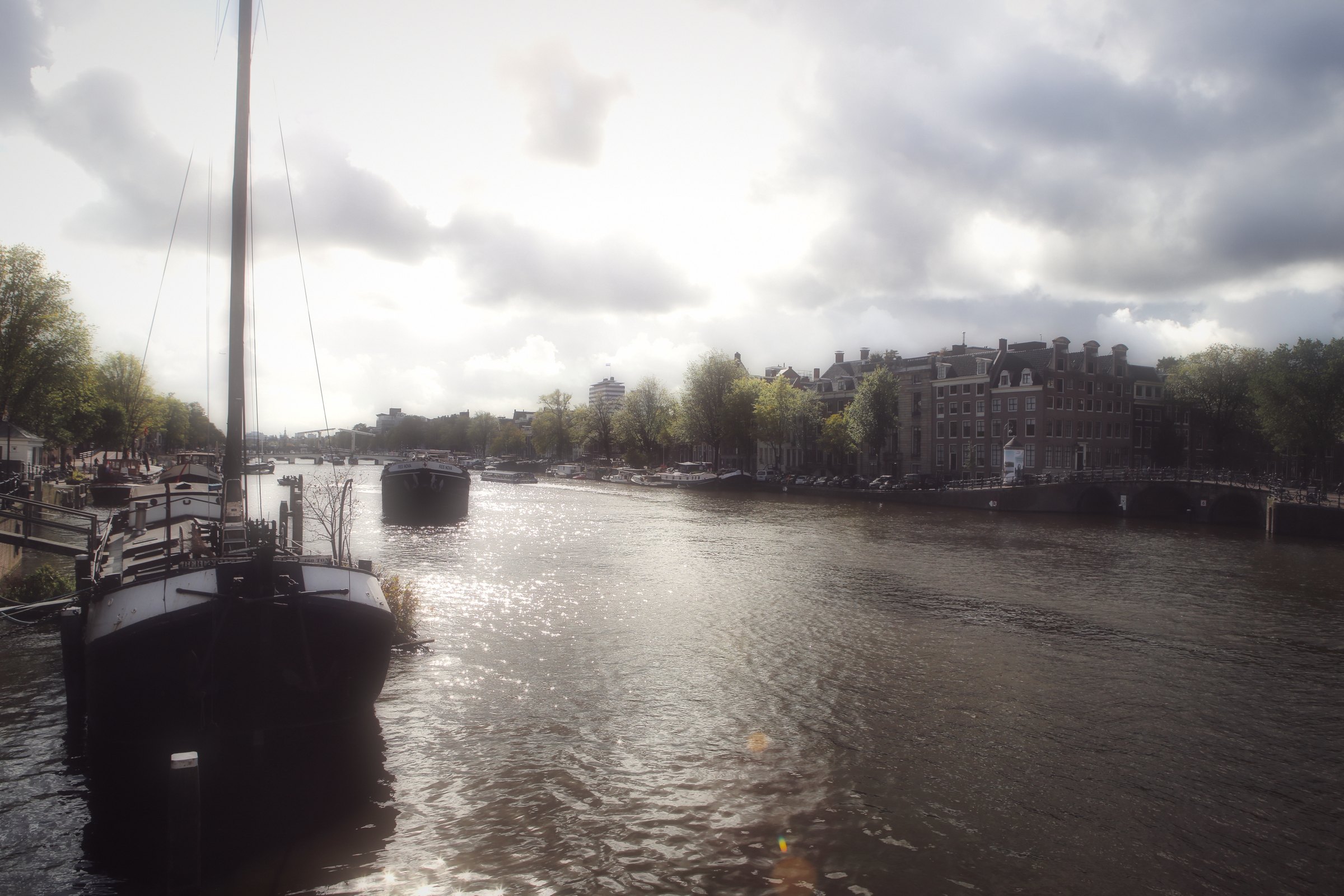 A moored sailing barge with a tall mast on wide grey water under cloud.