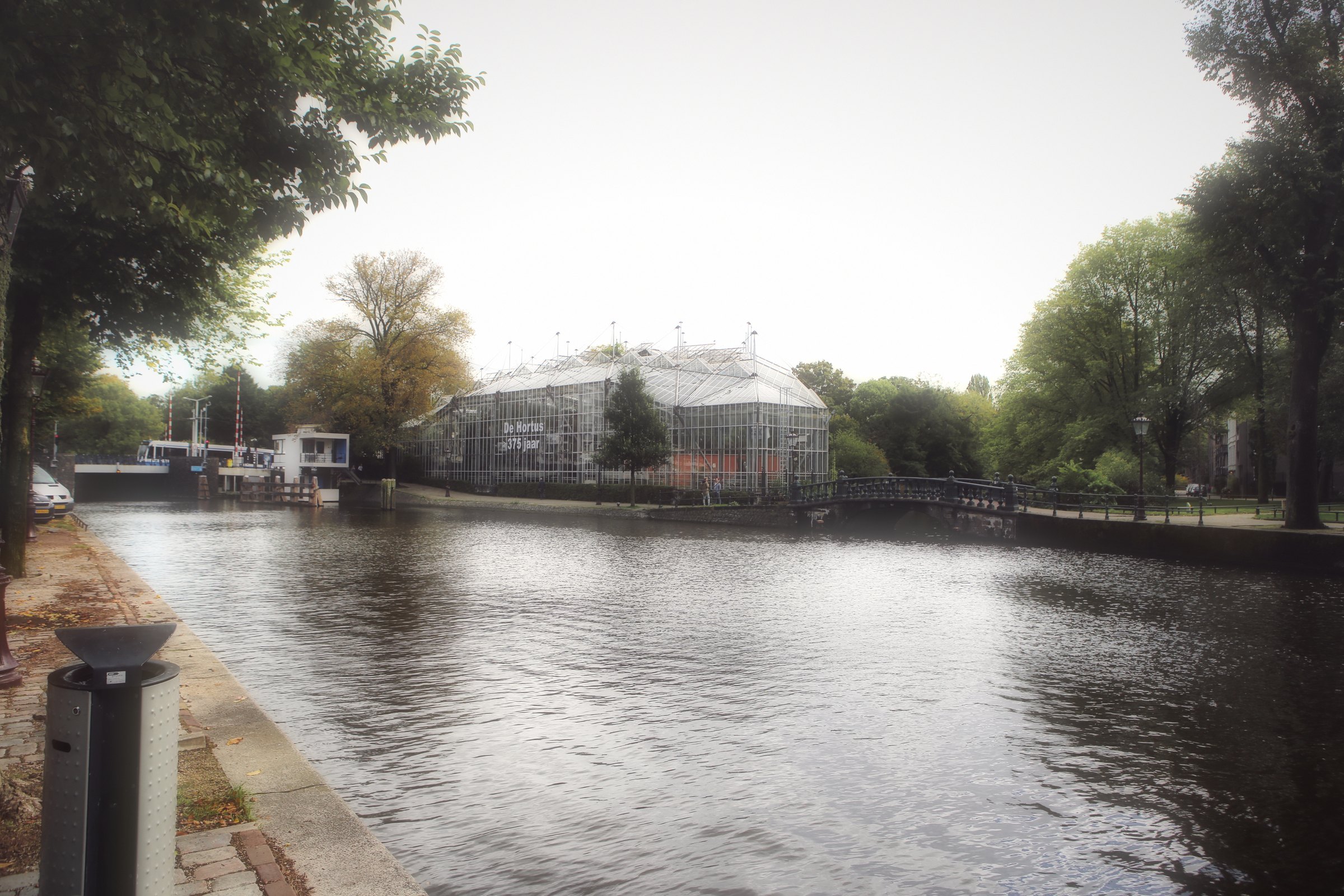A wide canal edged with trees and a bollard on a calm afternoon.