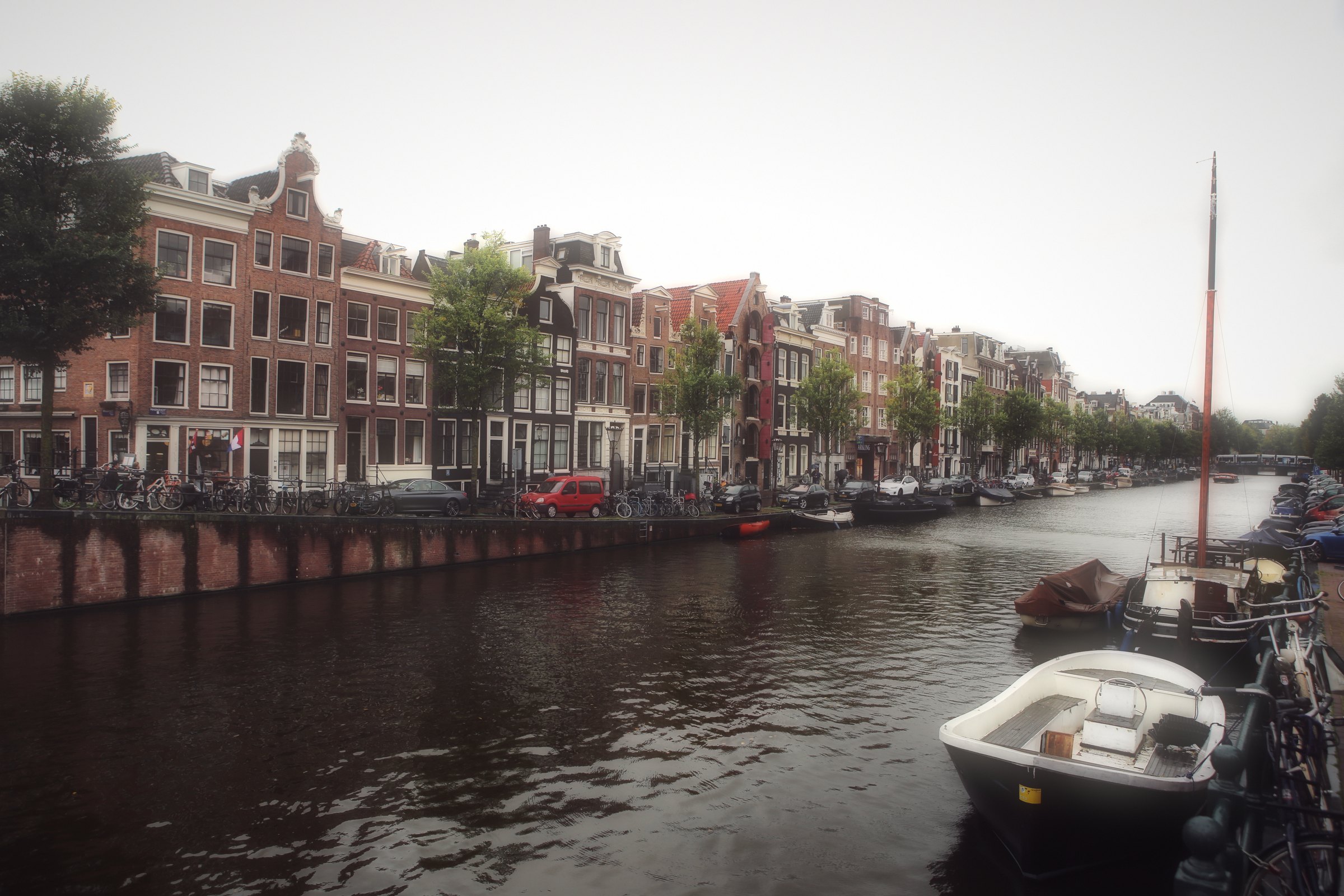 Brick canal houses and a moored boat across hazy water.