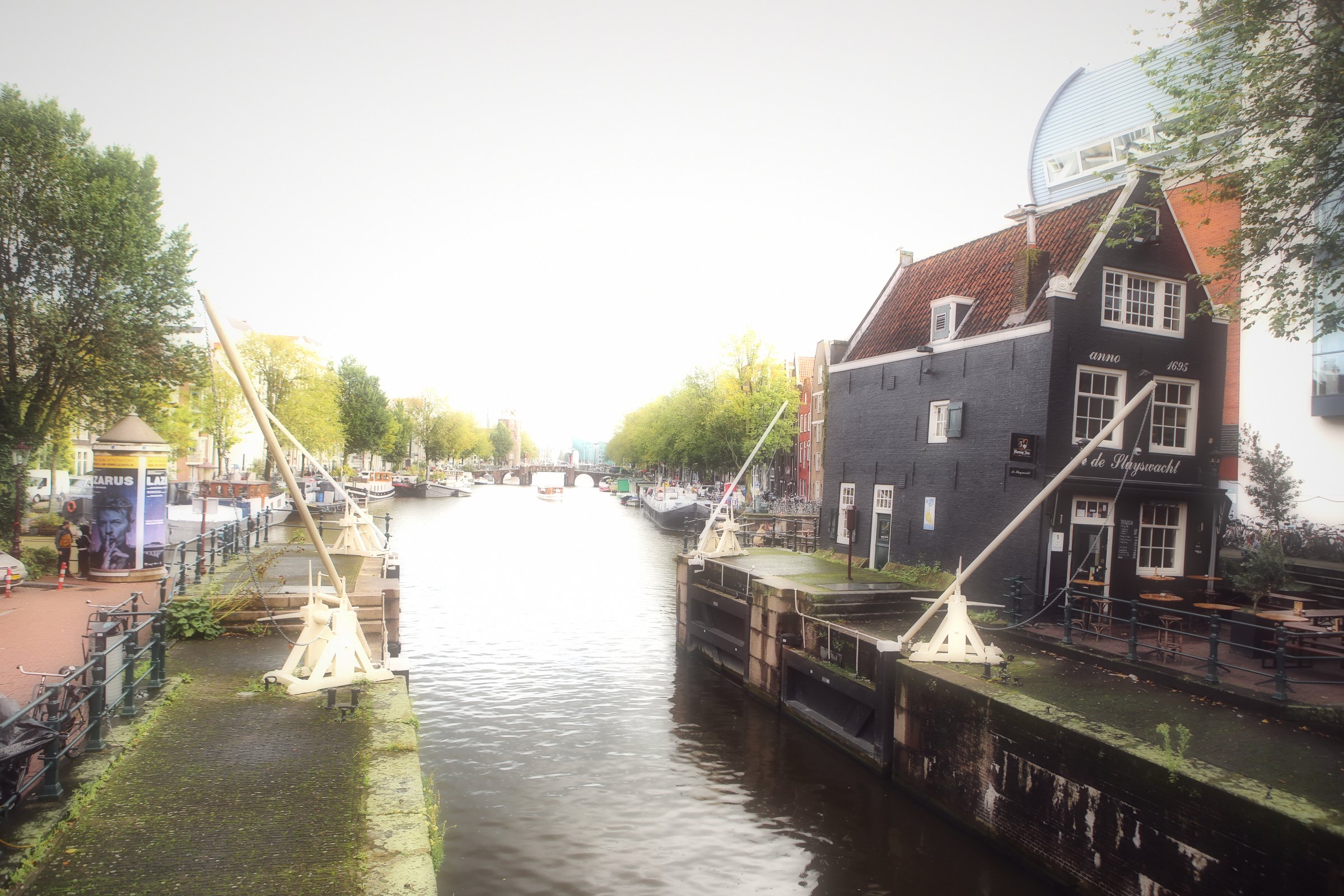 A dark wooden house beside a canal lock on a hazy afternoon.