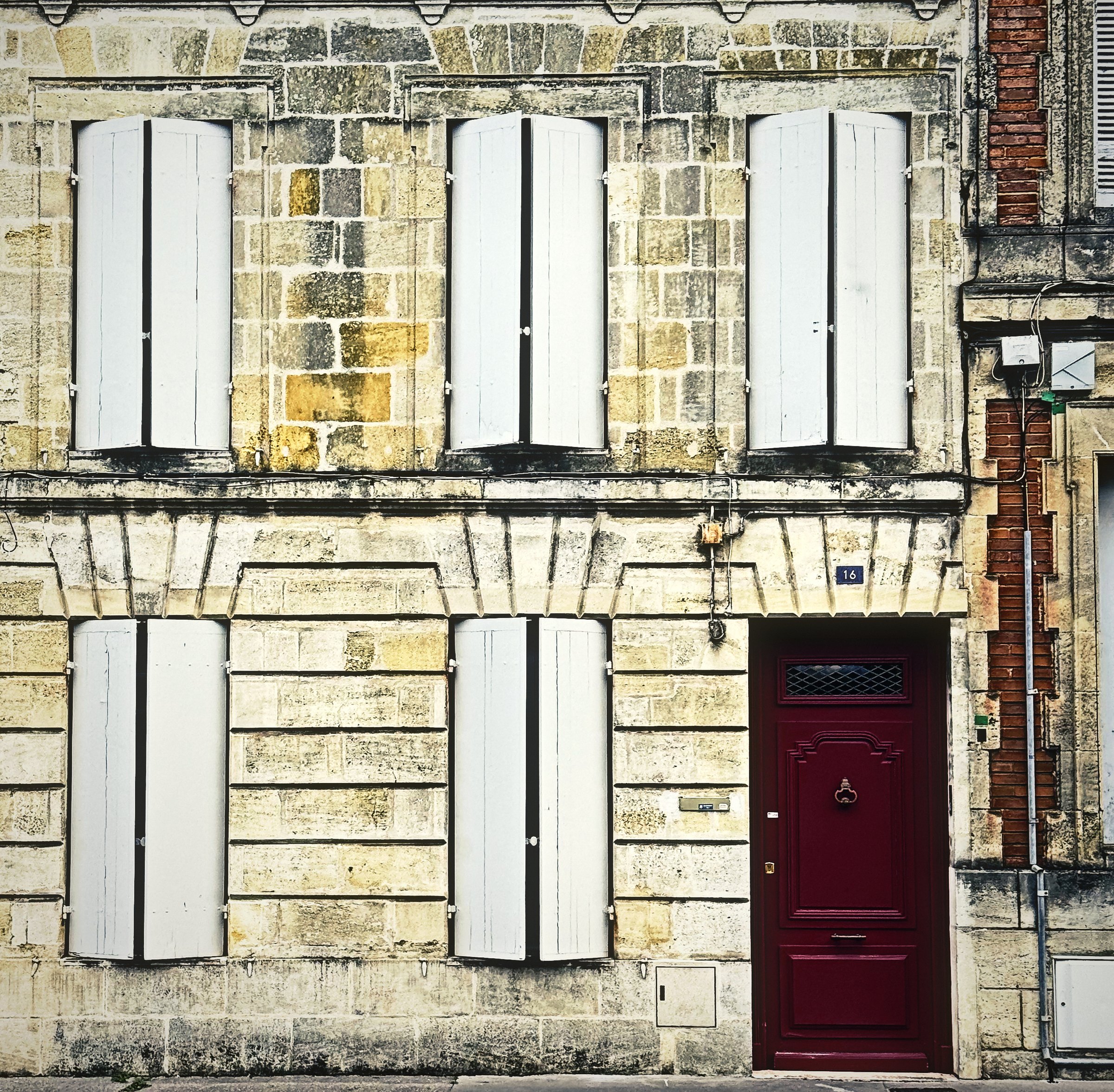 A limestone townhouse façade with six pale shutters and a deep red front door.