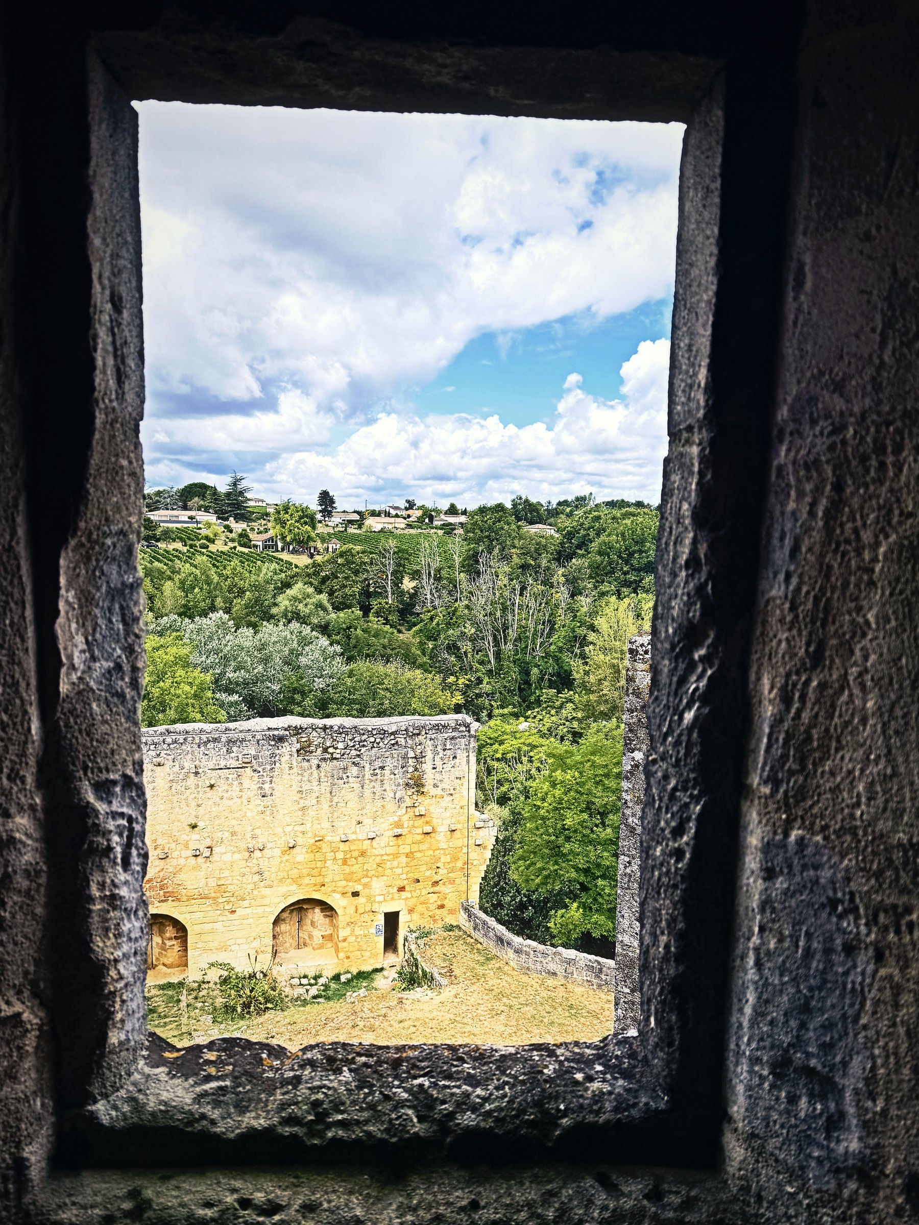 A deep stone window opening framing a view of green woods and a ruined wall below.