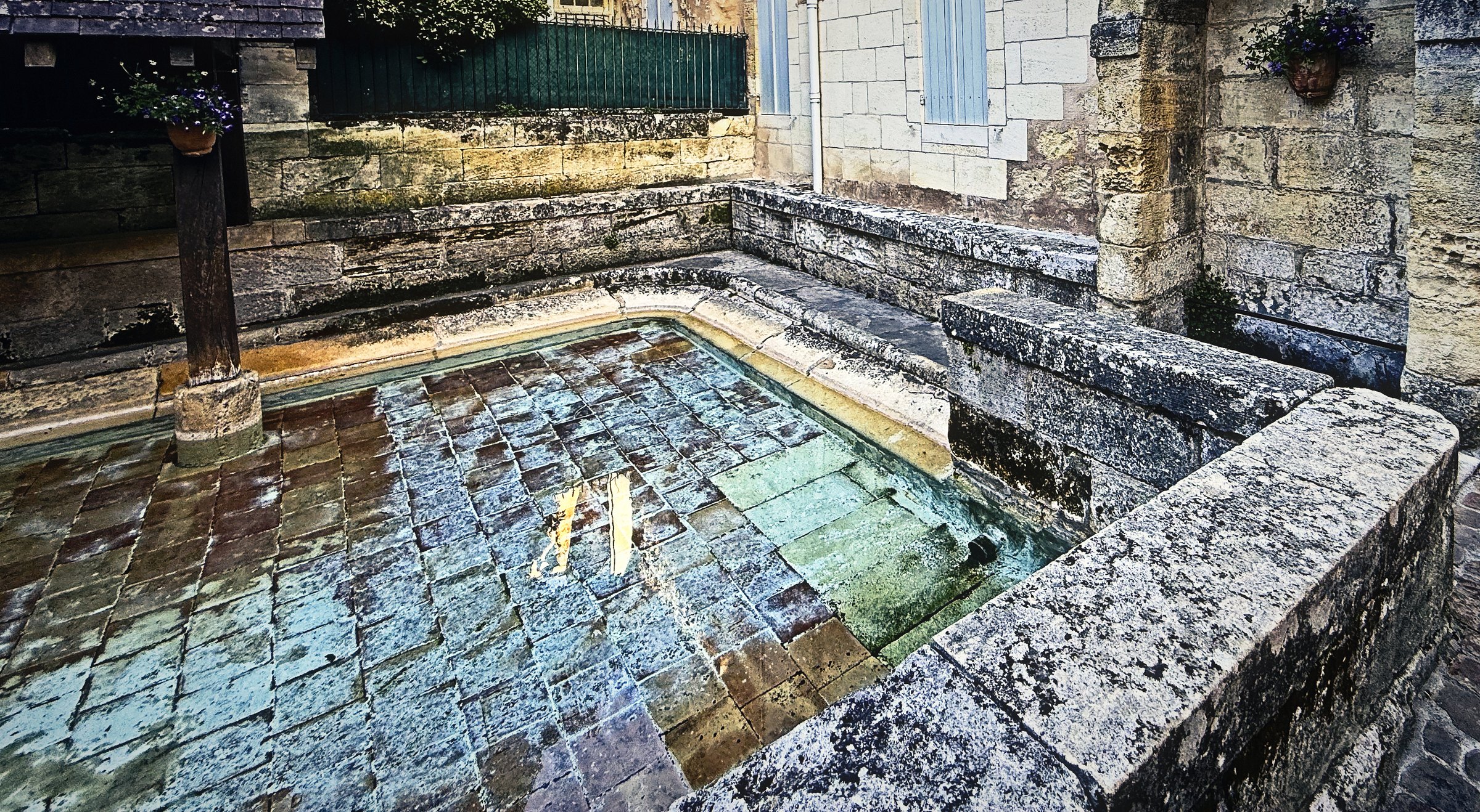 An old stone washing basin filled with clear water reflecting sky and stone.