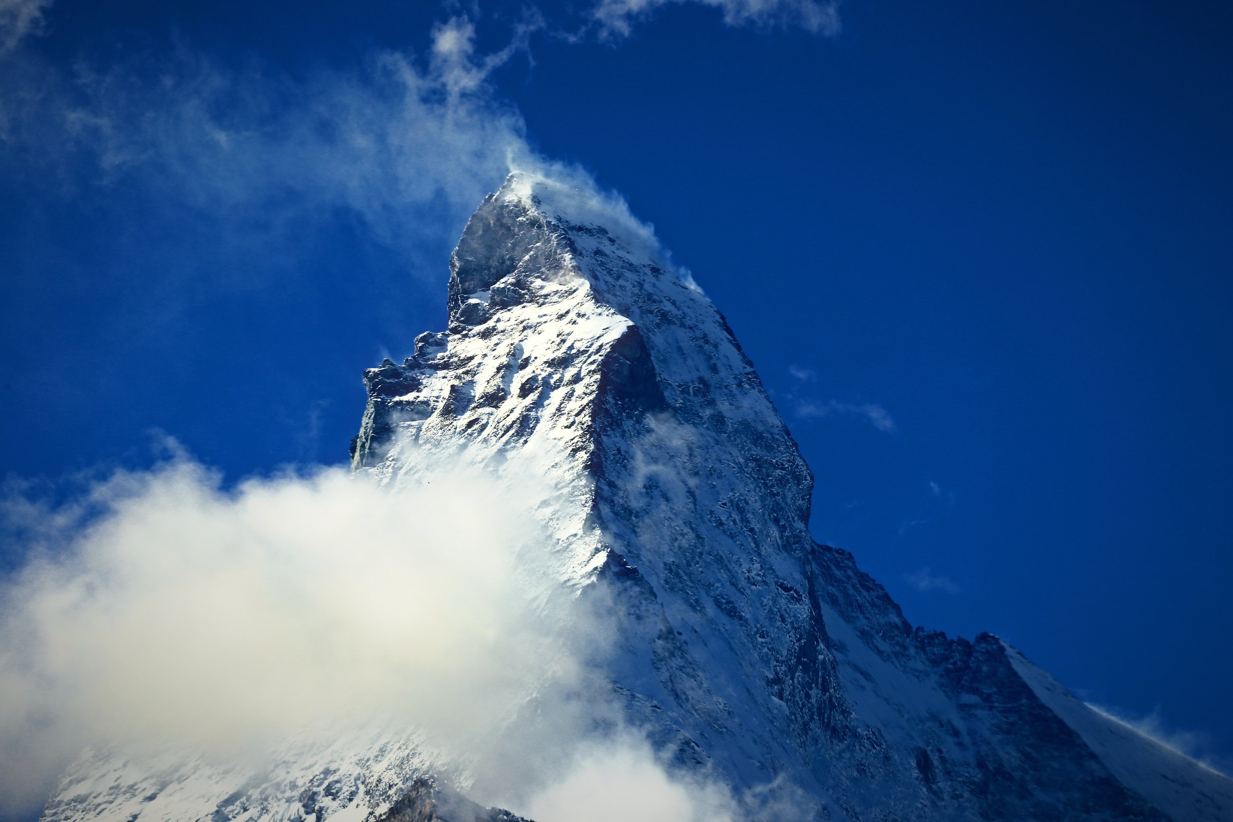 The Matterhorn trailing a plume of cloud off its summit into a deep blue sky.
