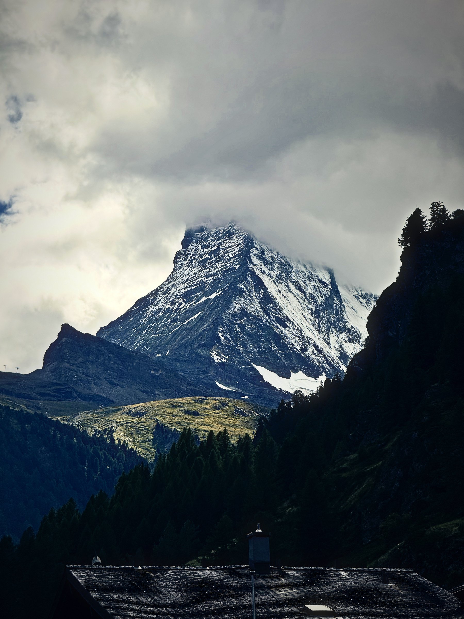 The Matterhorn partly hidden by cloud above dark fir trees.