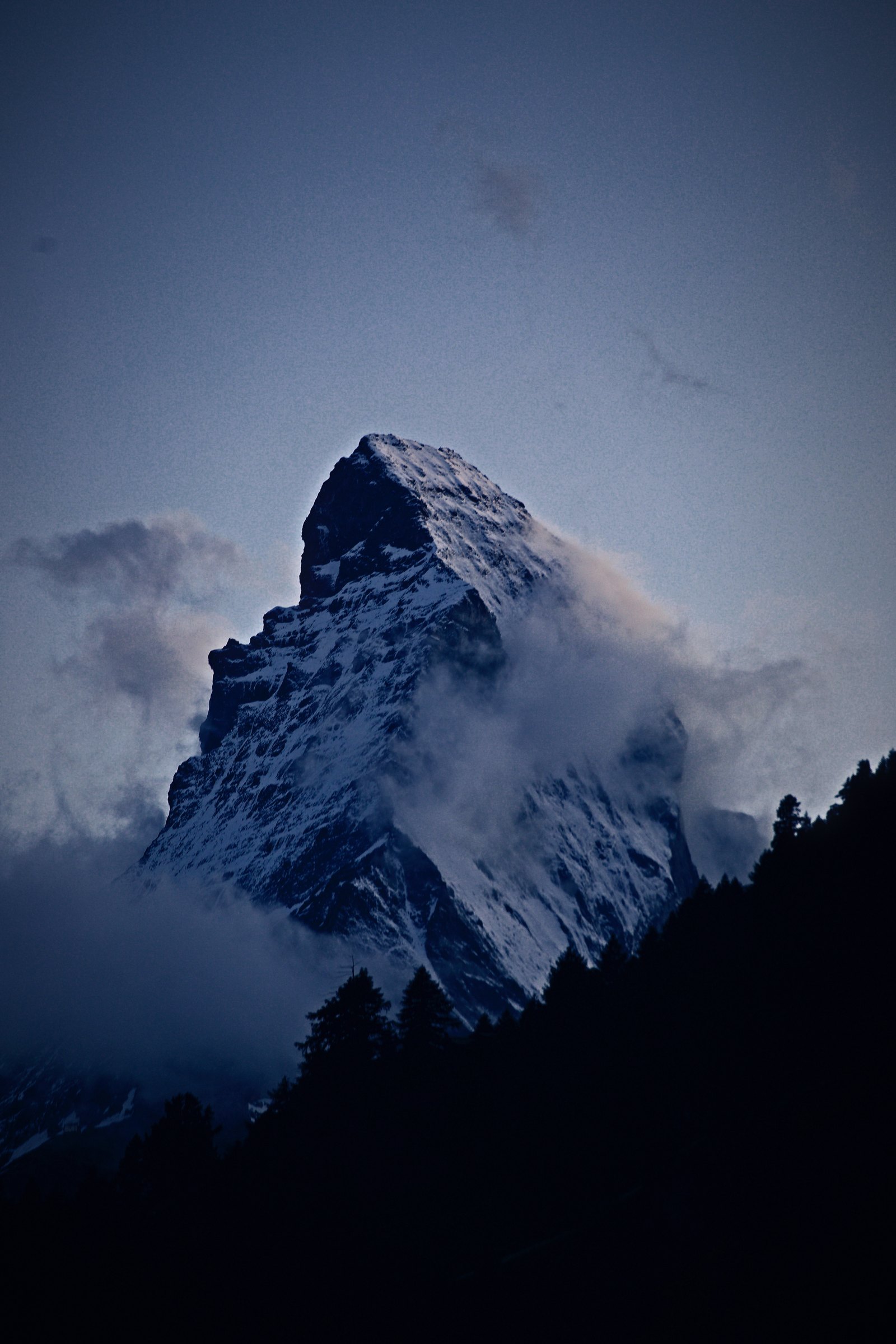 The Matterhorn emerging from mist and cloud in dim blue light.