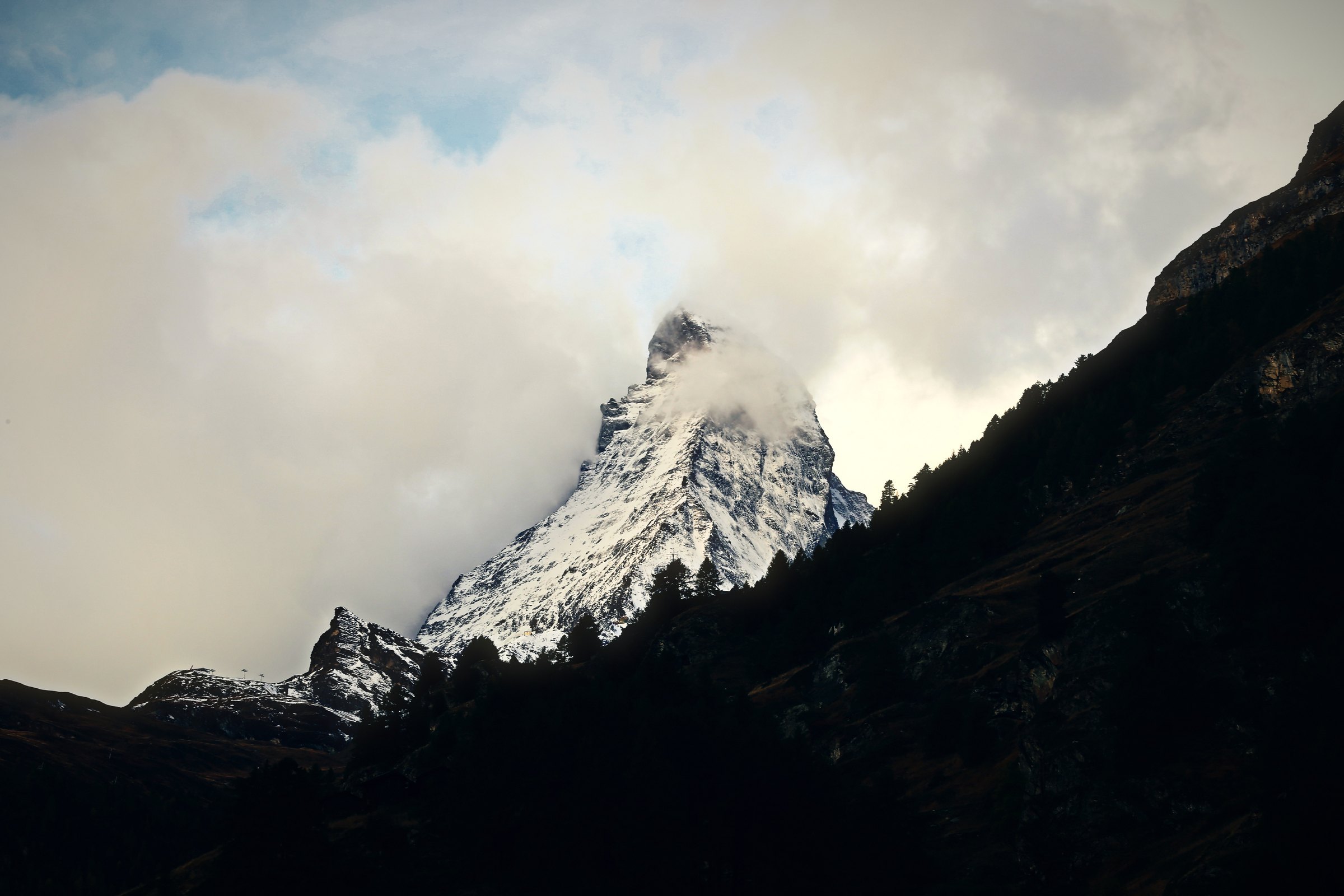 The Matterhorn's summit surfacing through glowing cream cloud above a dark ridge.