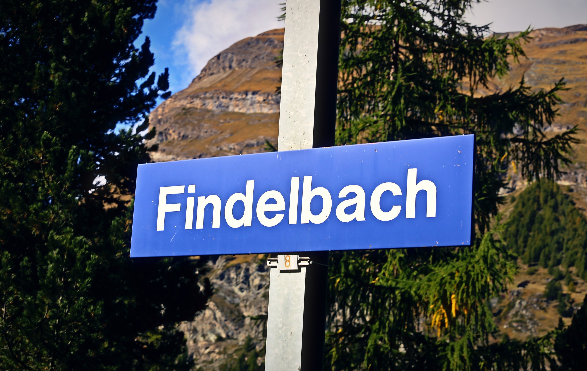 Blue station name board reading Findelbach against pines and a rocky peak.