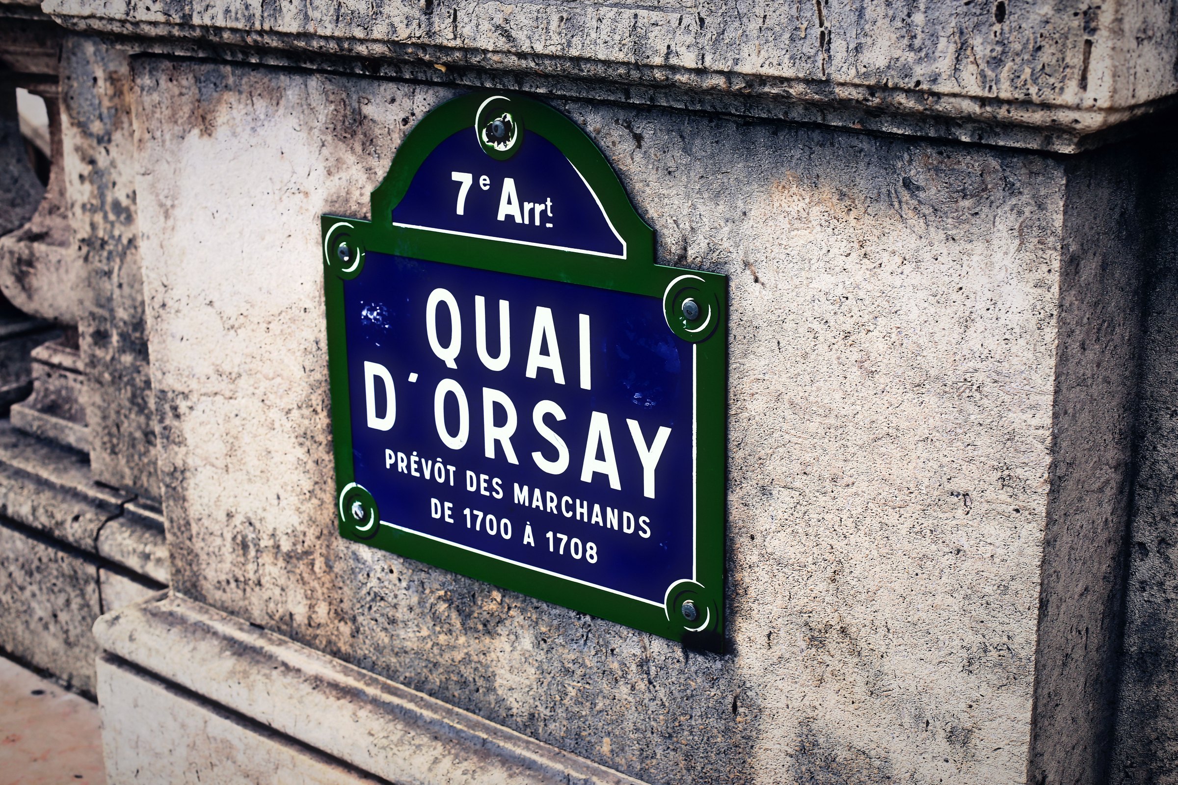 Enamel Paris street sign reading Quai d'Orsay with the dates 1700 to 1708 on pale stone.