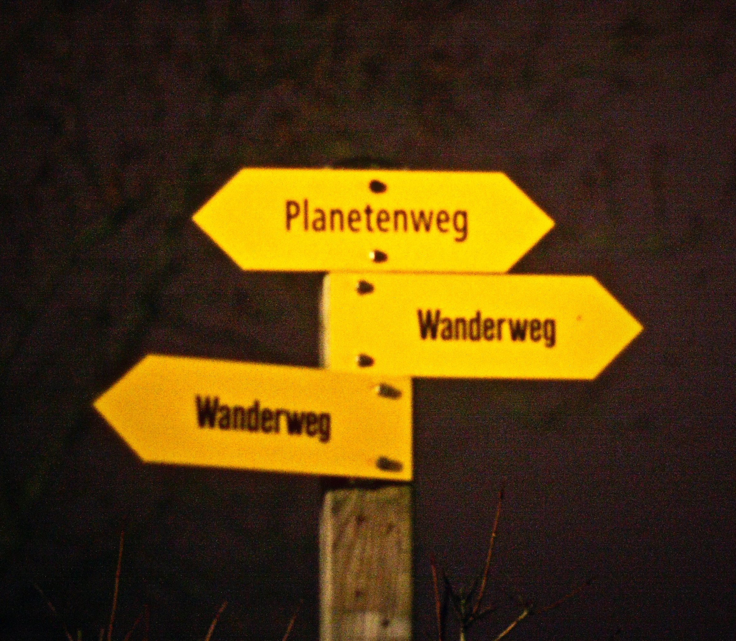 Three yellow Swiss hiking signposts pointing different ways against a dark background.