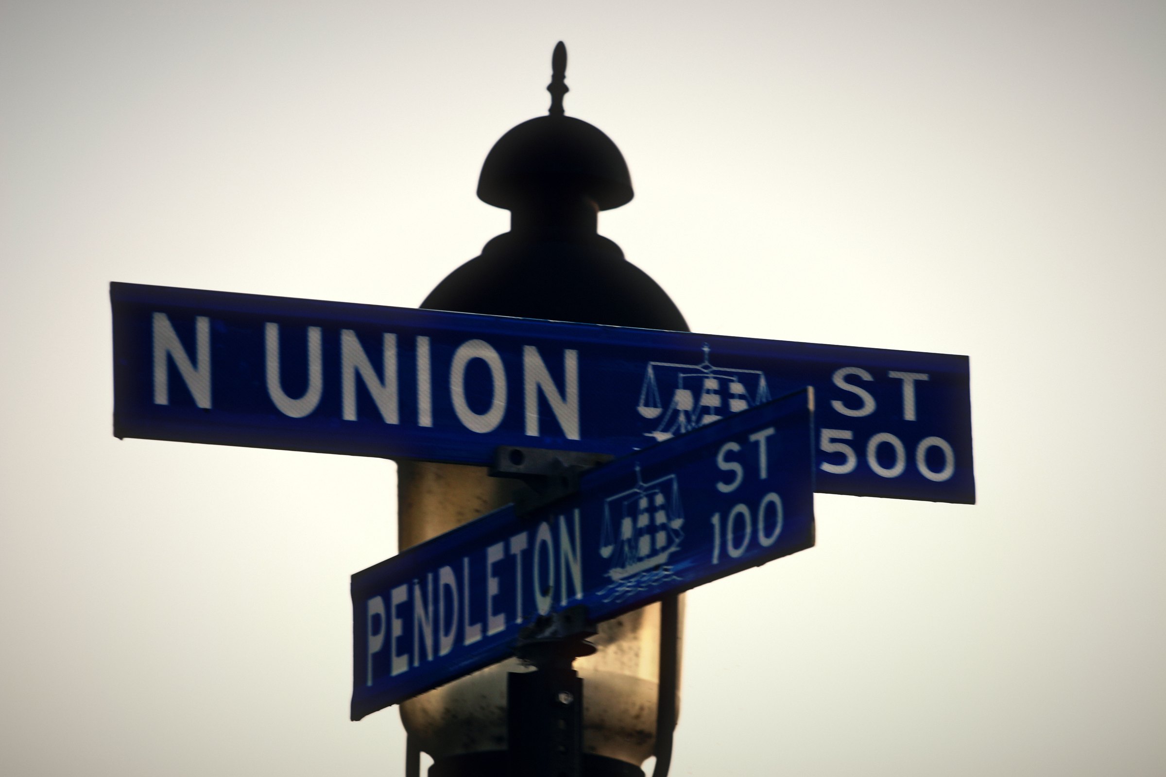 Blue street signs reading N Union St 500 and Pendleton St 100 crossing in front of a lamp.