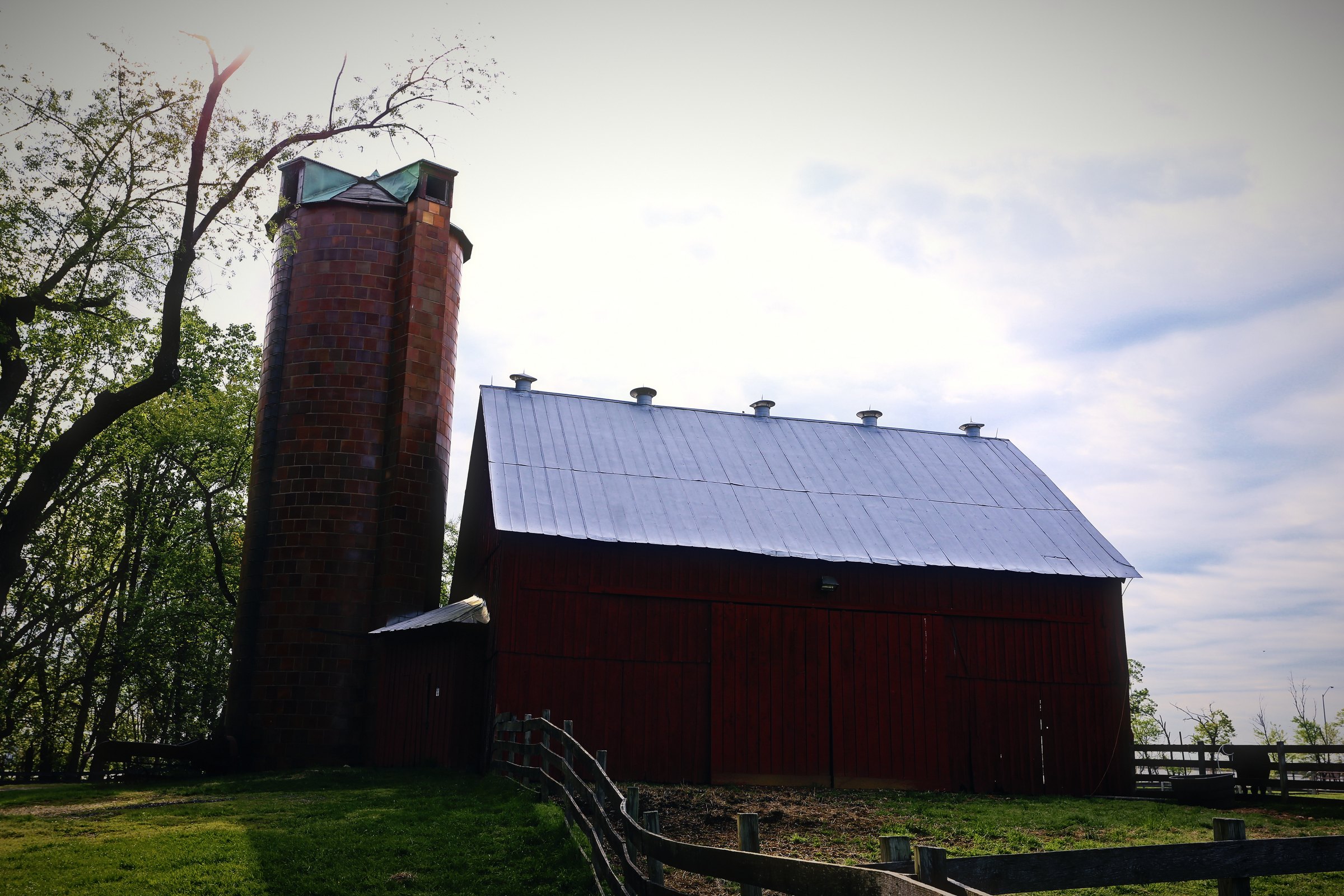 A red barn with a white roof beside a tall brick silo under a pale sky.