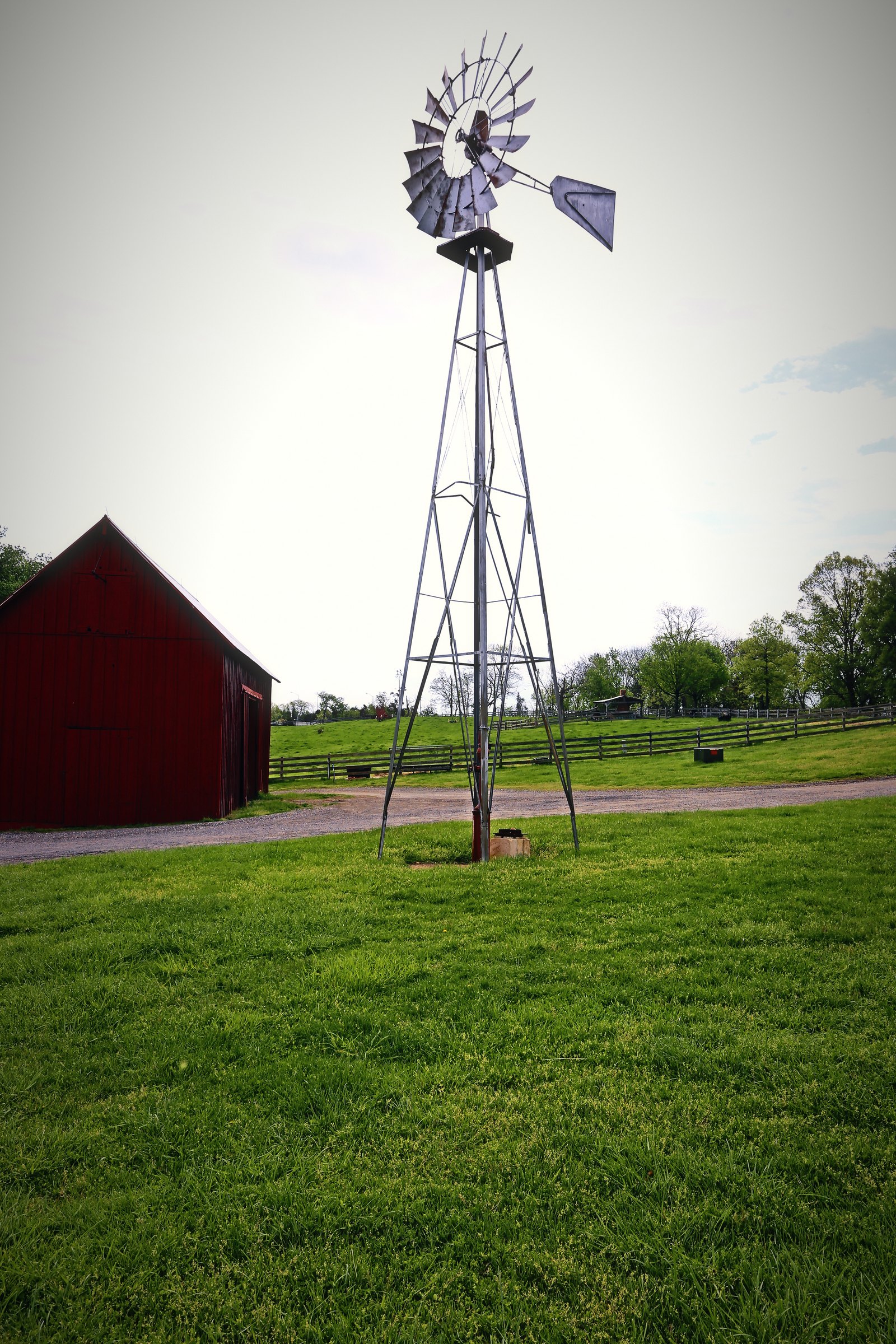 A metal windmill on a tall frame beside a small red barn on a green lawn.