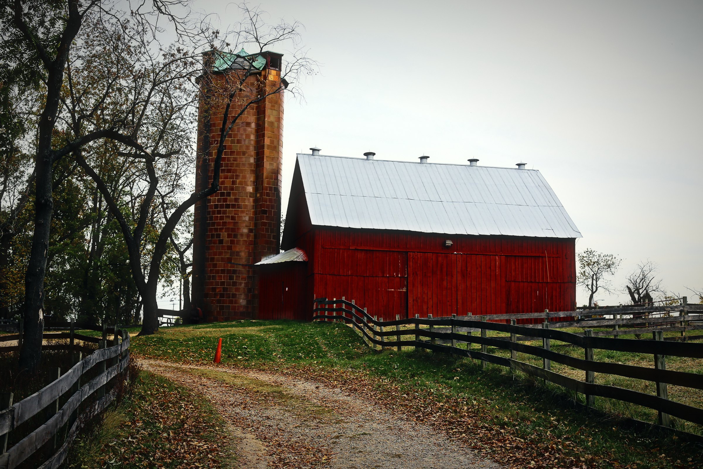 A red barn and brick silo at the end of a dirt lane with wooden fencing.