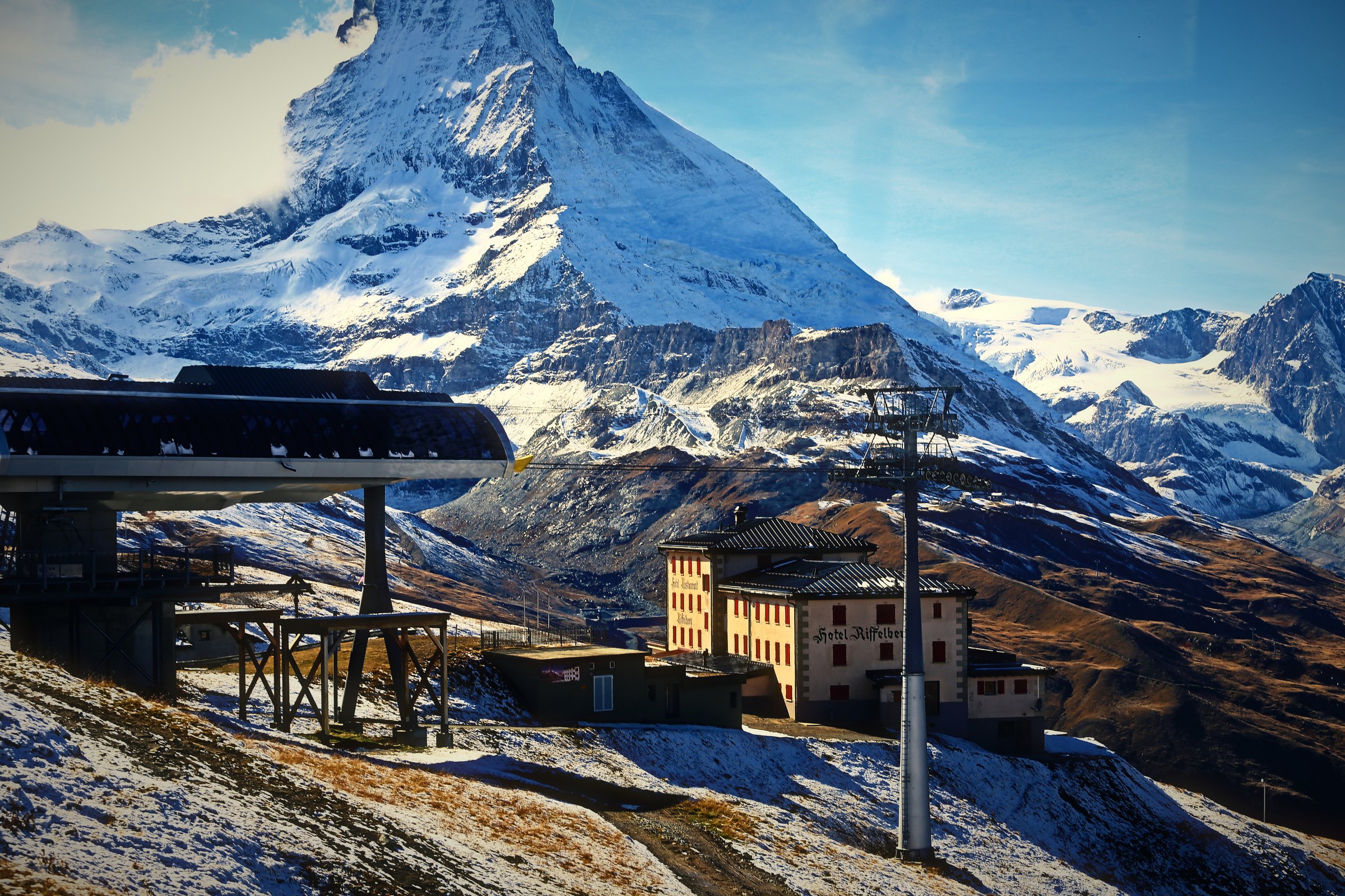 A wooden alpine building with red shutters below the snowy Matterhorn.