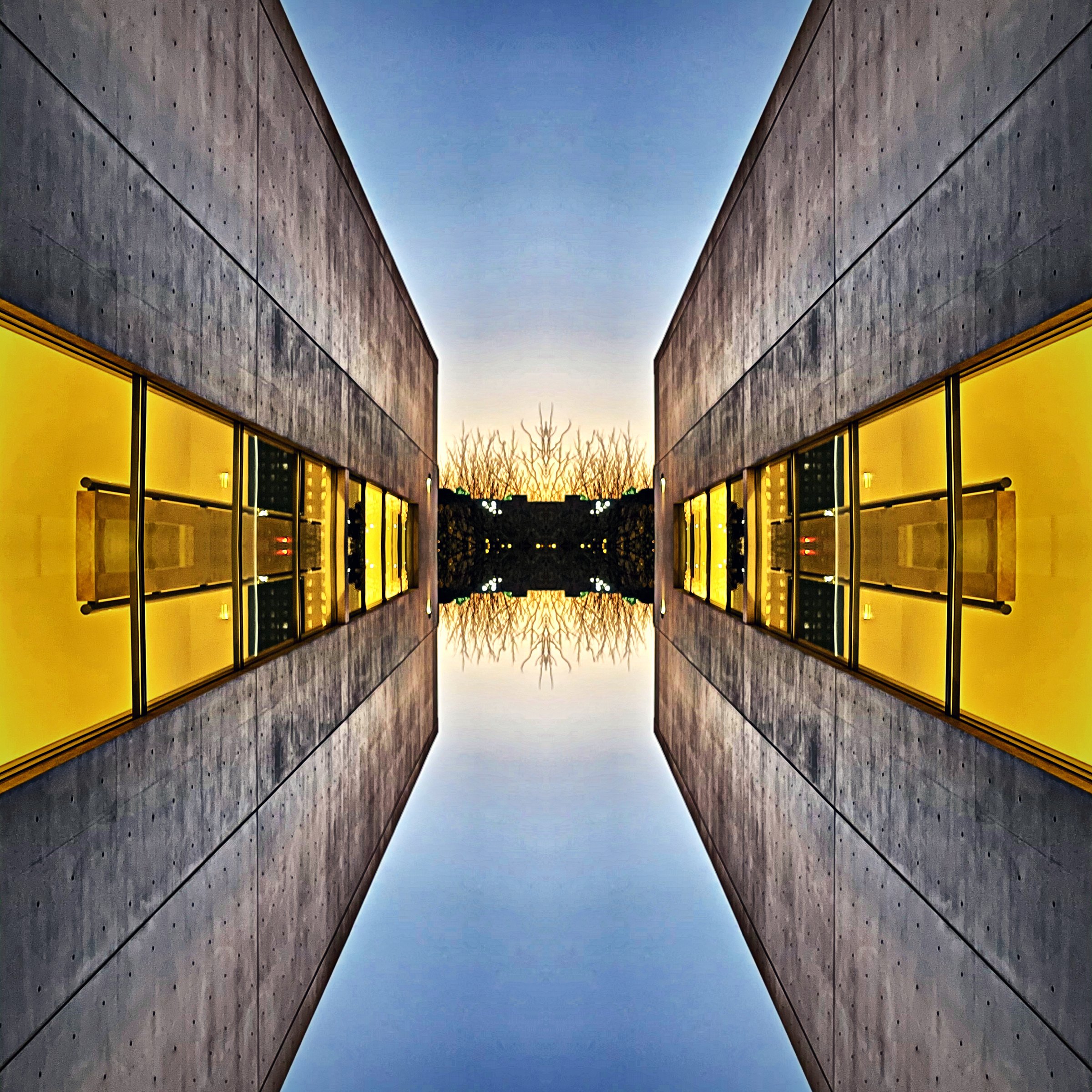 Symmetrical corridor of gold and glass mirrored over still blue water.