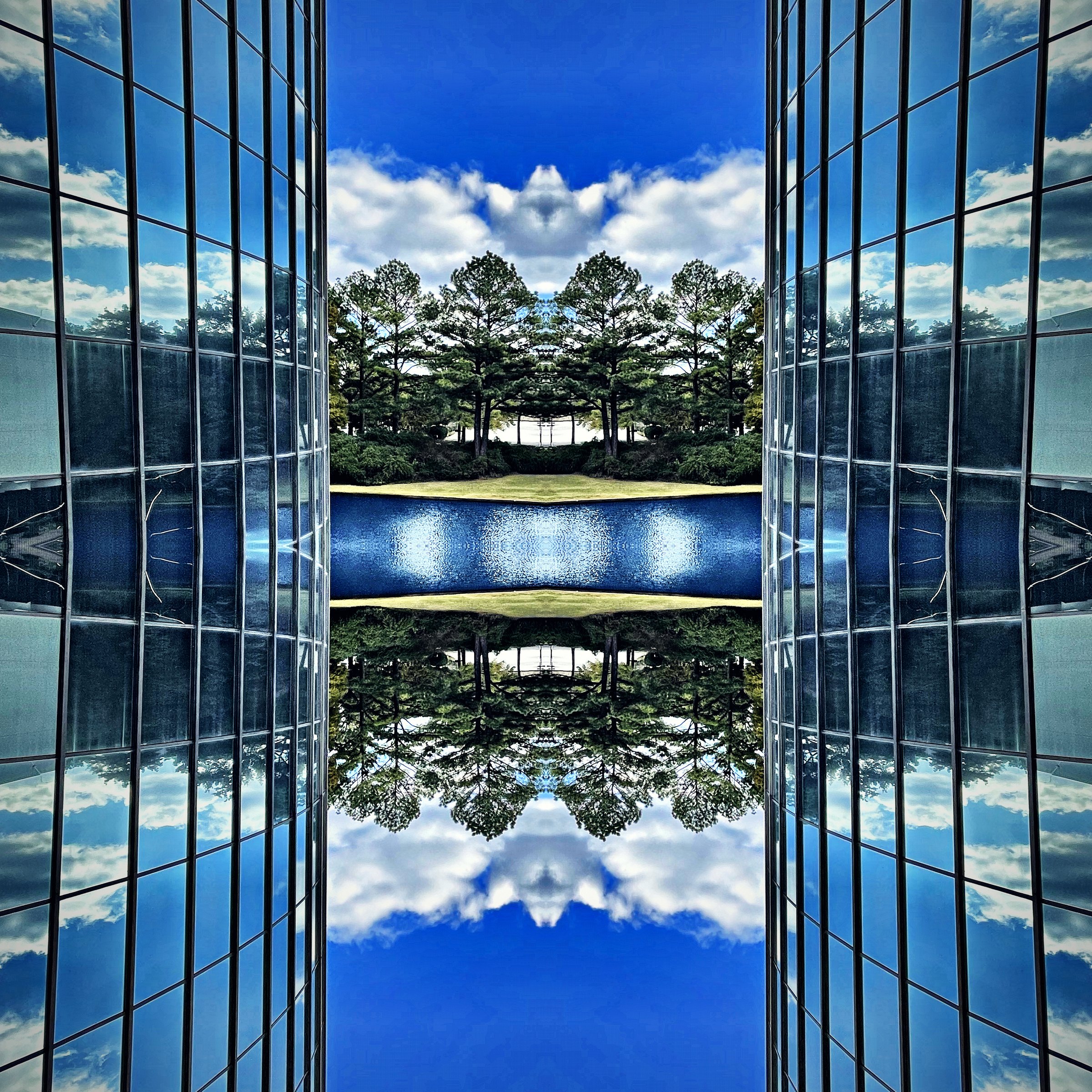 Glass towers and trees mirrored into a symmetrical blue reflection.