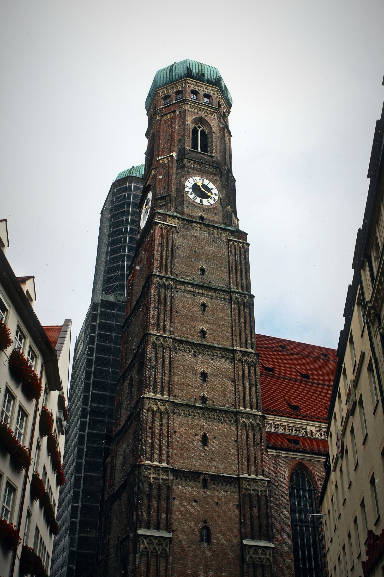 Brick church tower with a clock and green domed top above a narrow street.