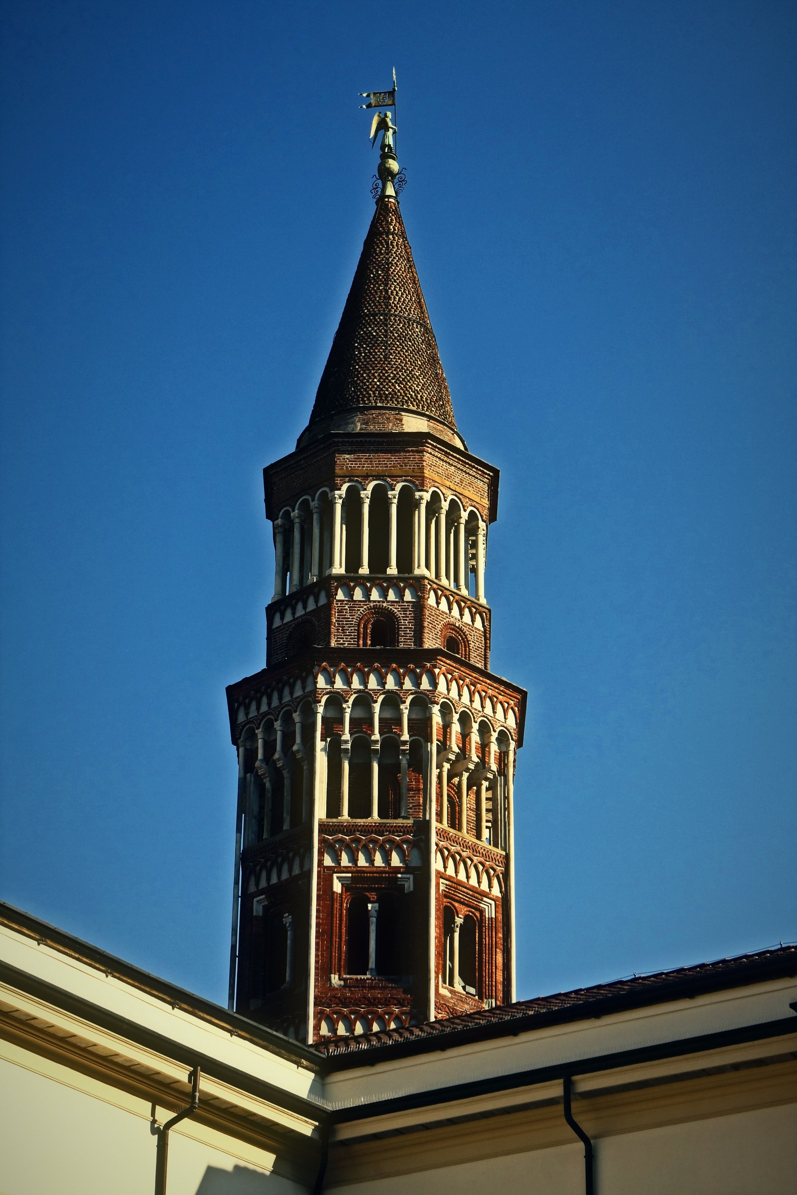 Brick and stone bell tower with a conical top under a clear blue sky.