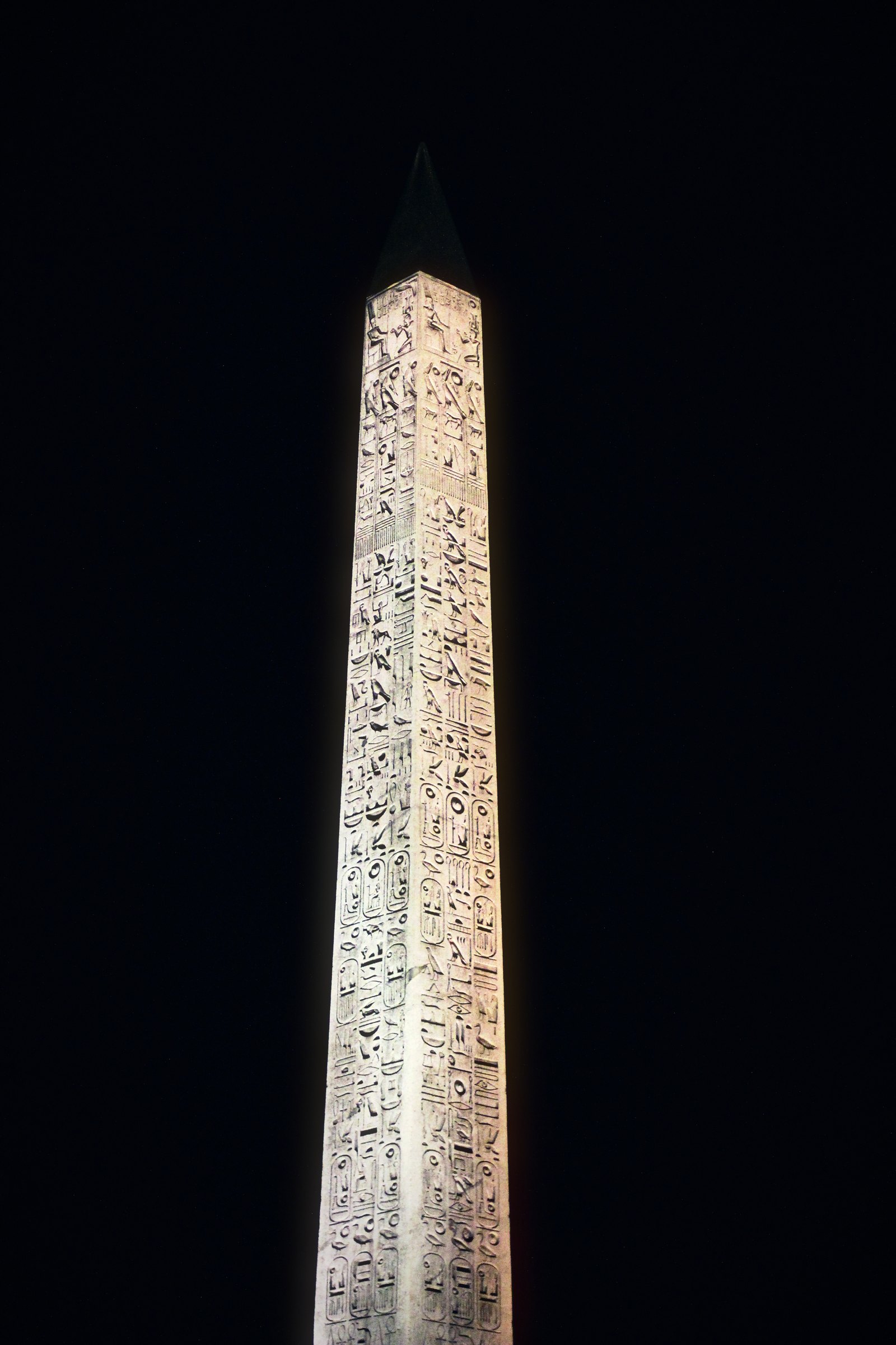 Carved stone obelisk glowing against a black night sky.