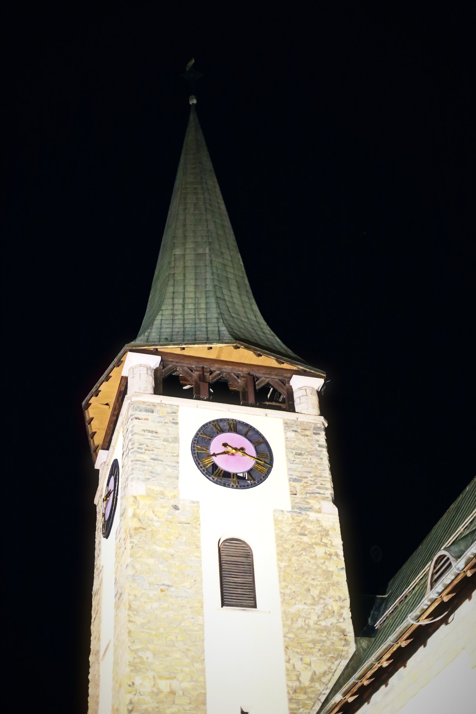 White church clock tower with a green spire against a dark sky.