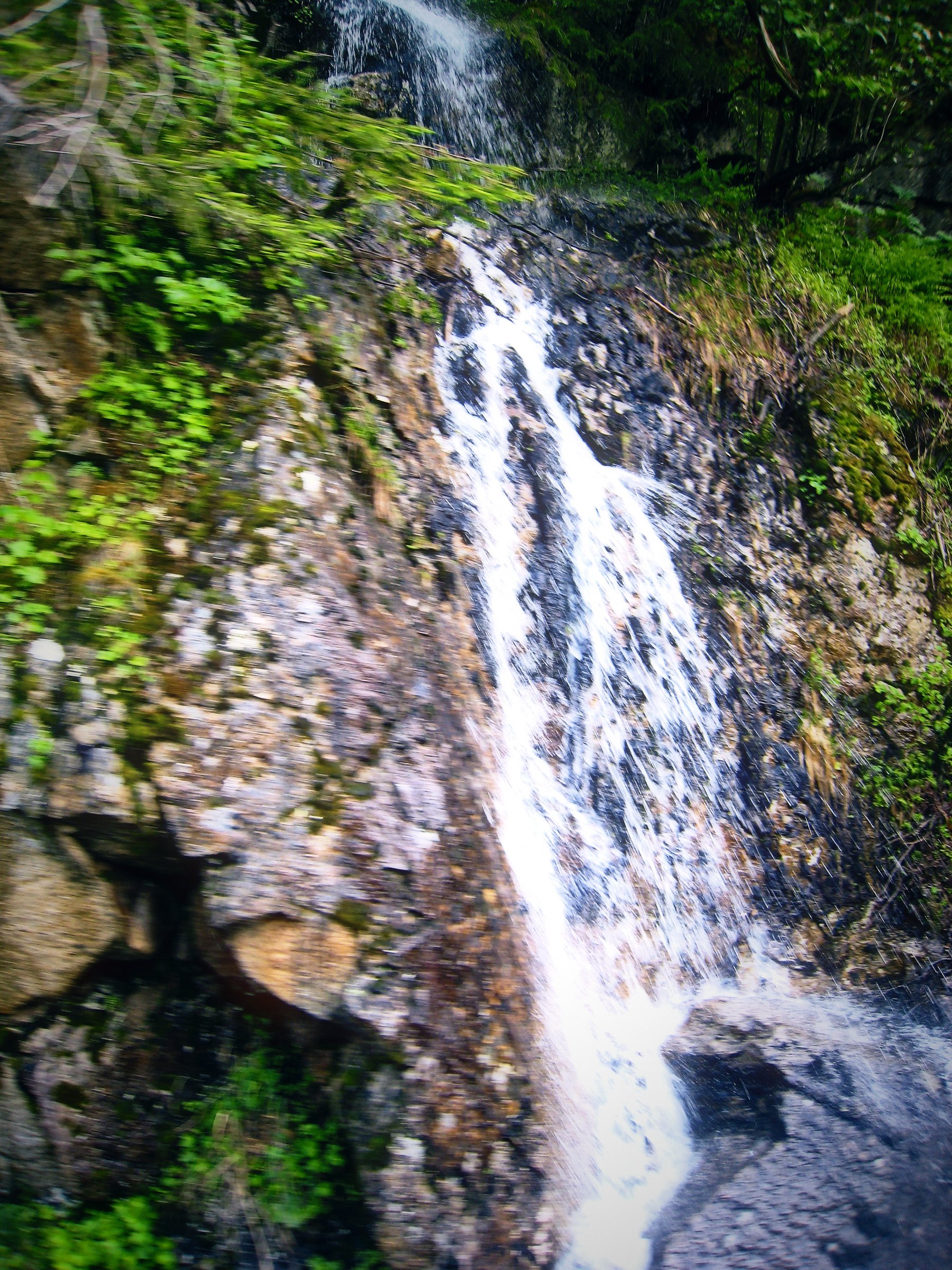 A tall, narrow waterfall threading down a dark mossy cliff.