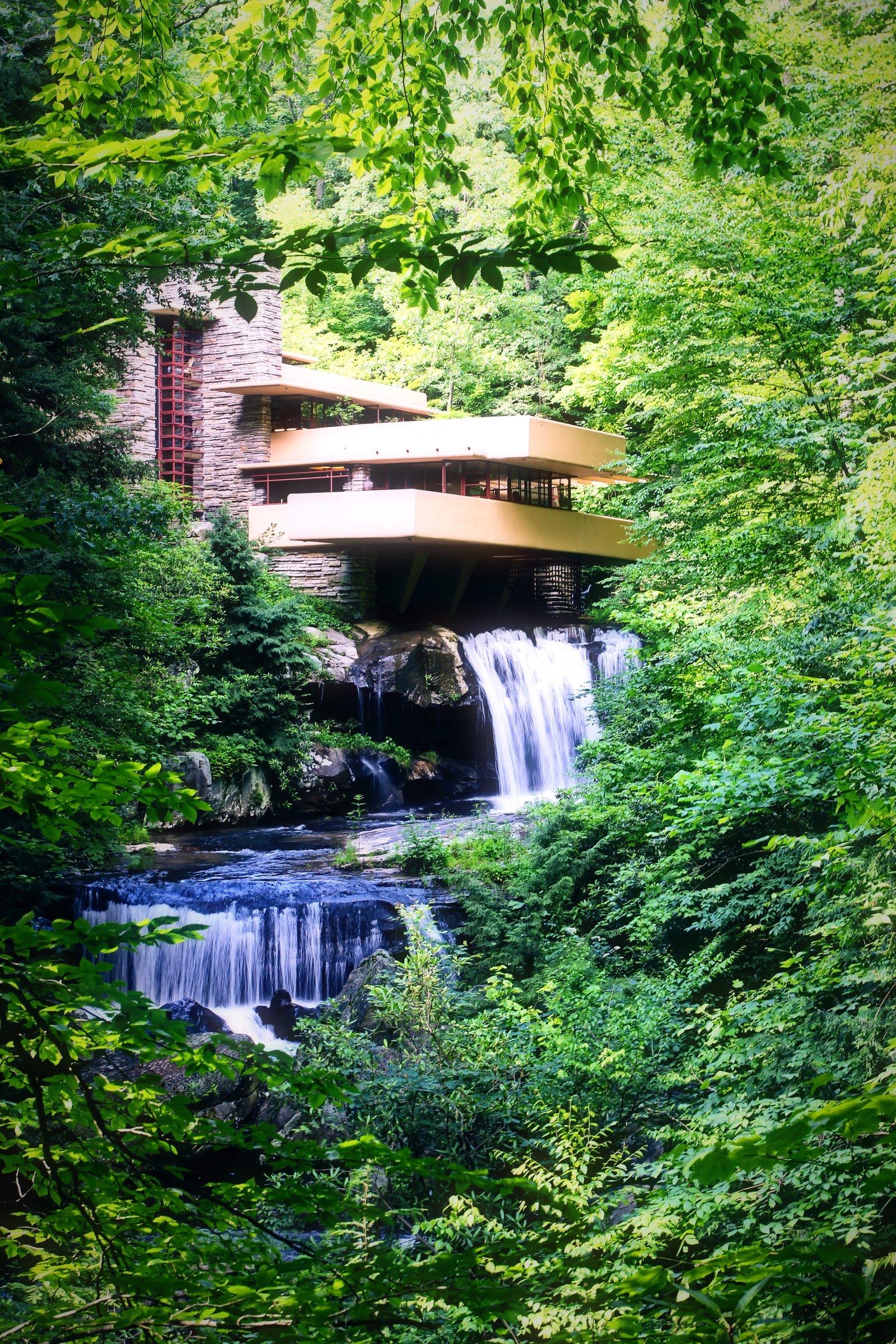 A cantilevered house above a small waterfall in a deep green forest.