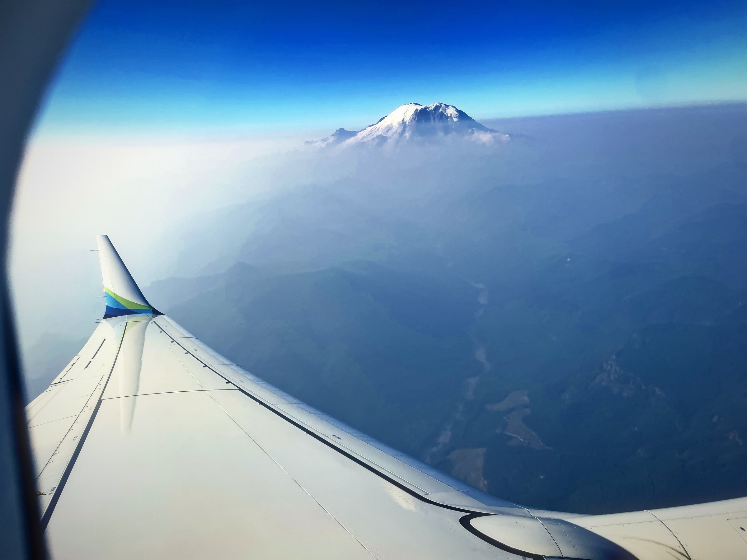 Snow-capped Mount Rainier floating above blue haze beyond an airplane wing.