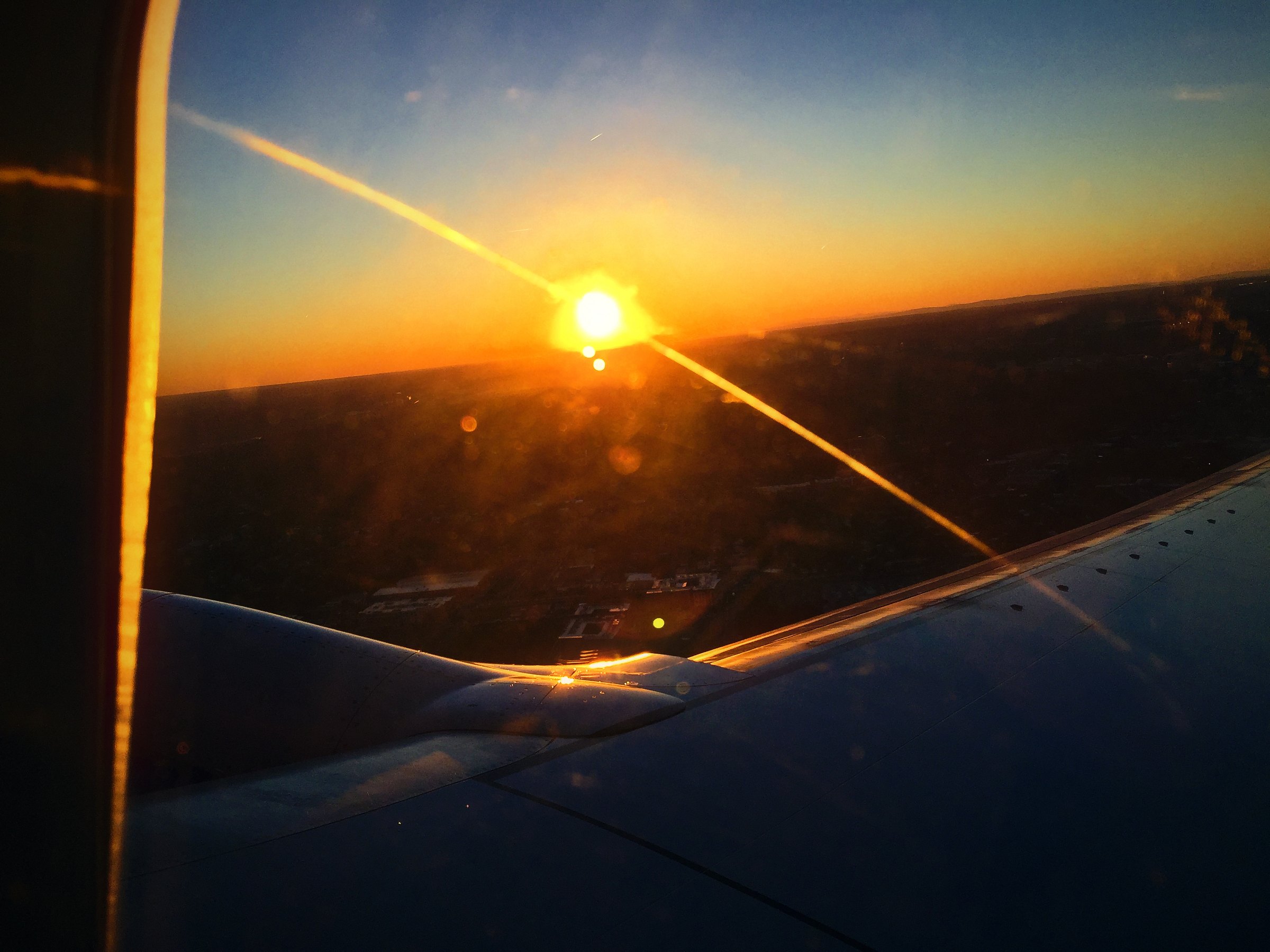 Low sun bursting through an airplane window, with a gold streak across the wing.
