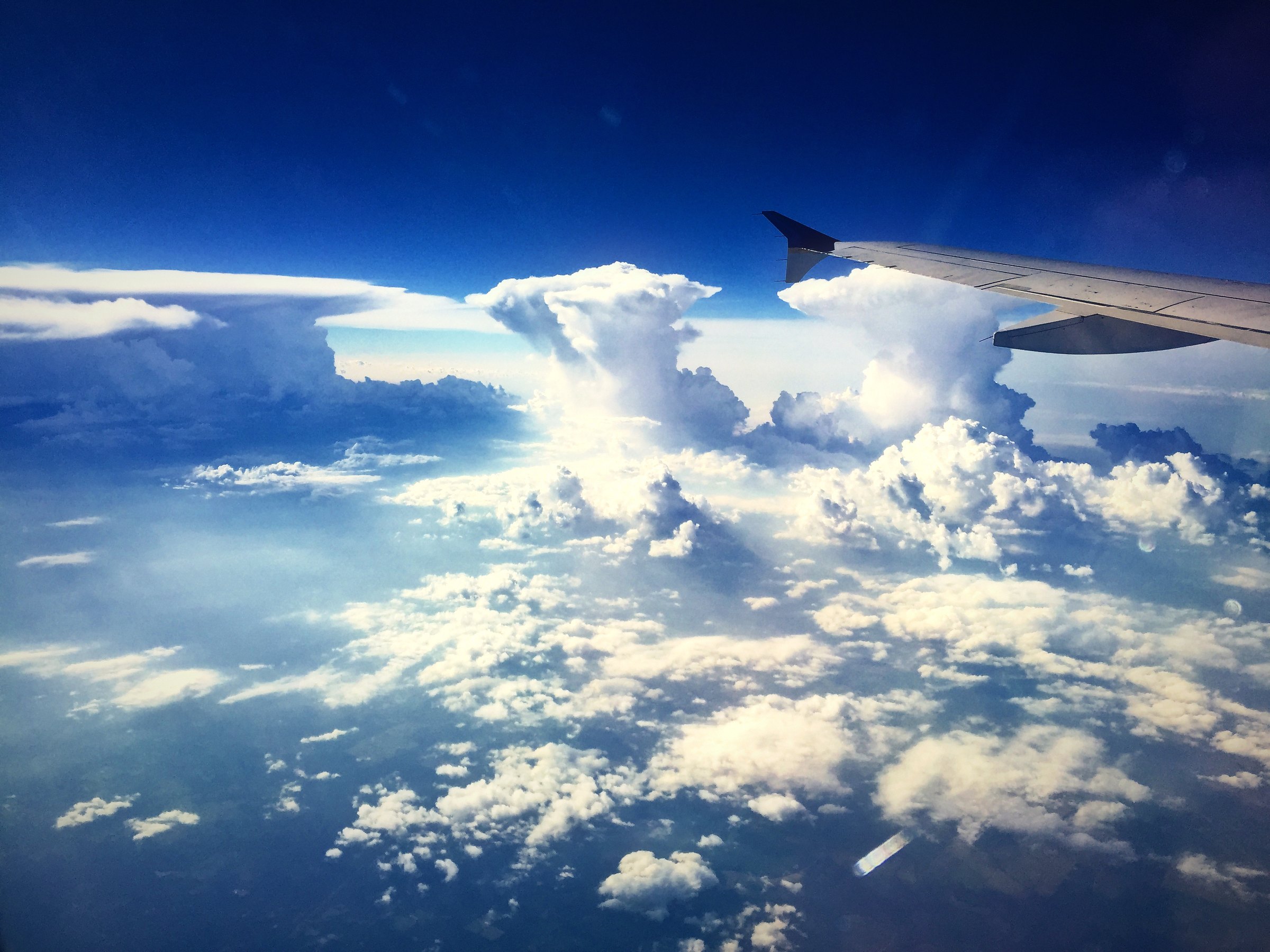 Summer cumulus clouds stacked across the sky below an airplane wing.