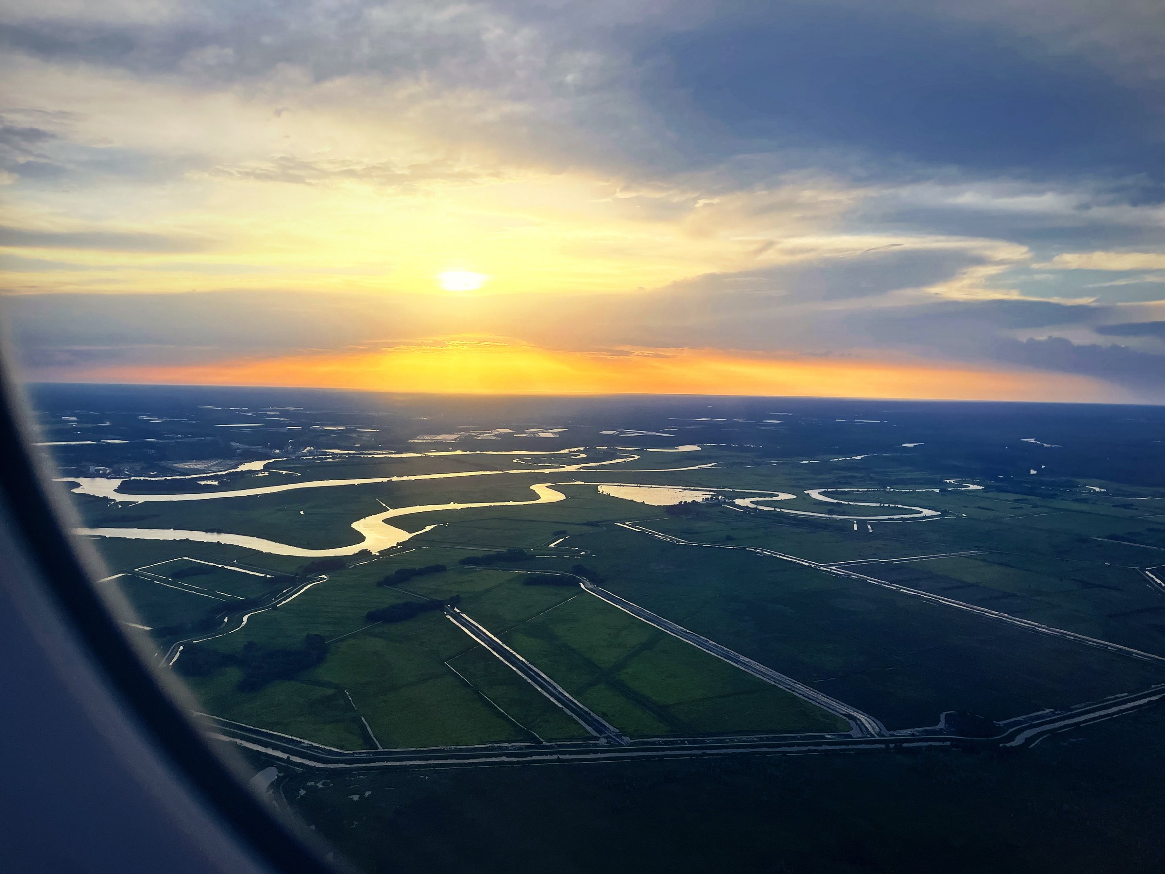 Winding river and wetlands seen from the air with the sun setting on the horizon.