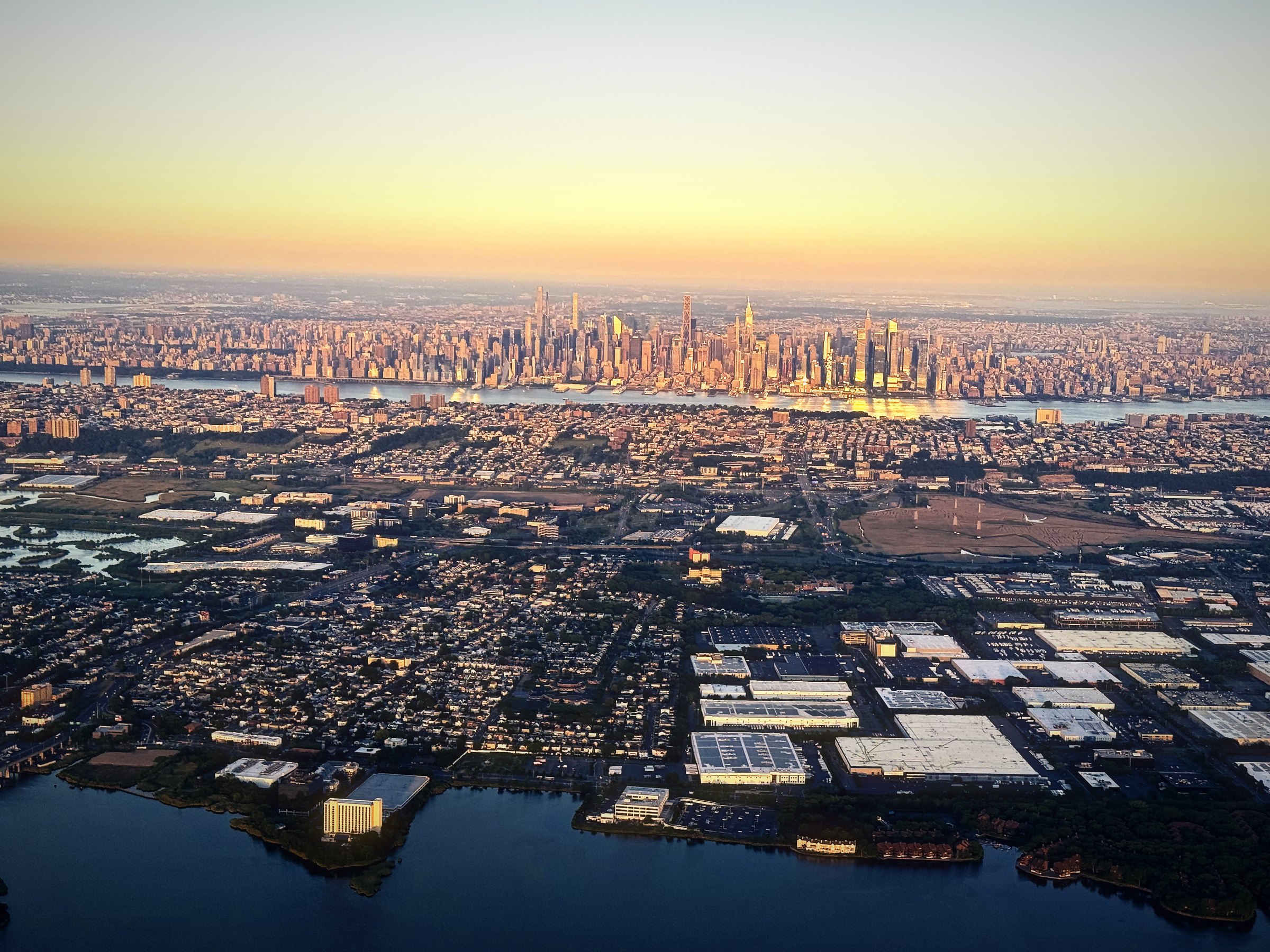 The Manhattan skyline on the horizon in golden evening light, seen from the air over New Jersey.