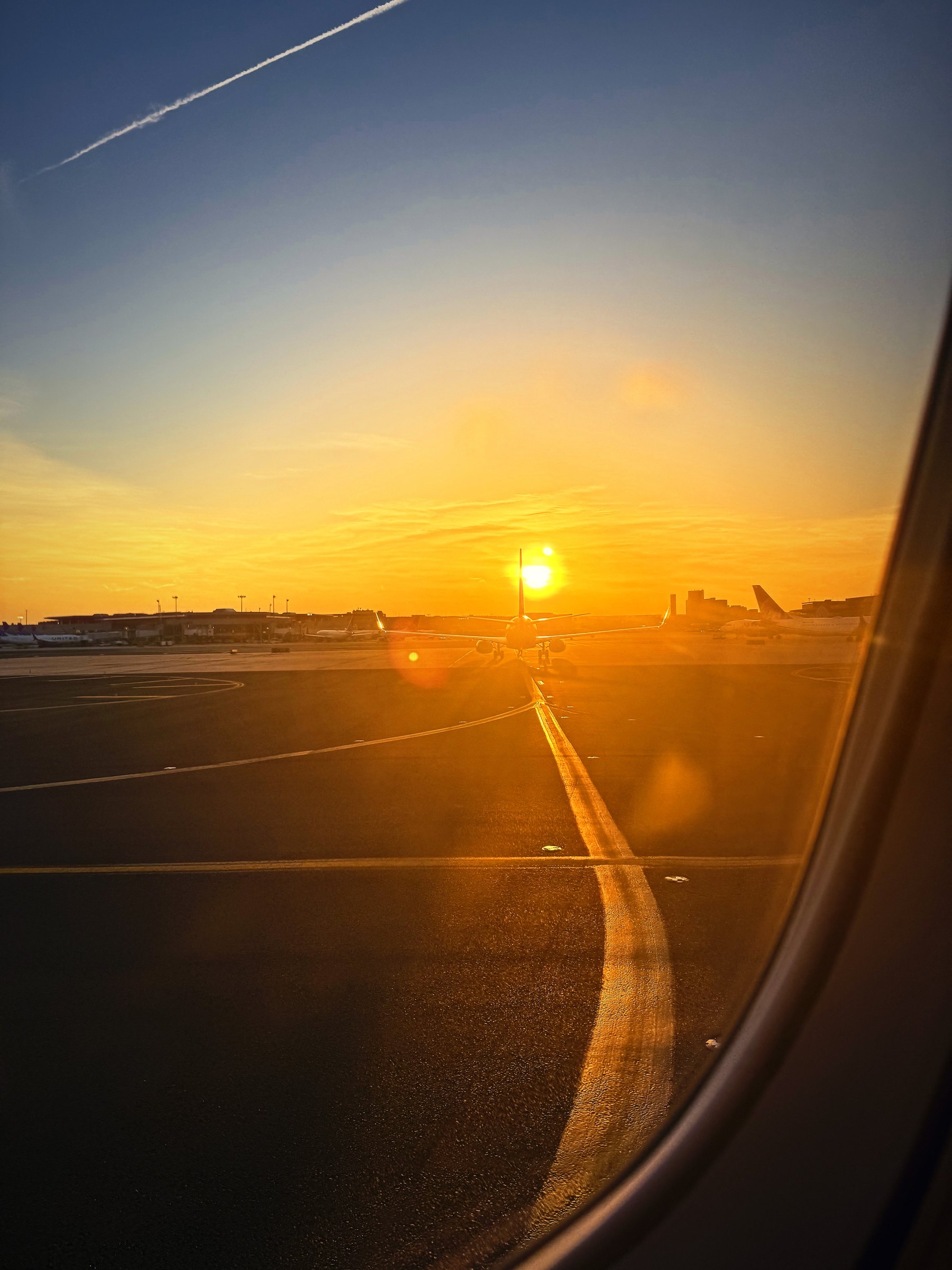 Sun setting over an airfield, with a curving taxiway line seen through the window.