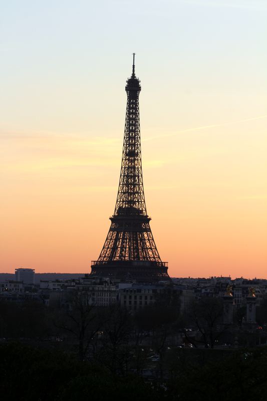 Eiffel Tower silhouette against pale apricot twilight sky.