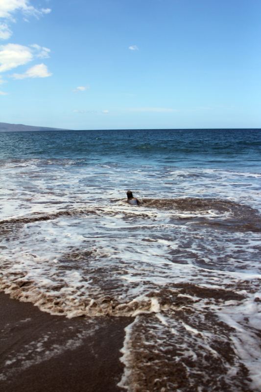 White foam washing over dark volcanic sand under blue sky.
