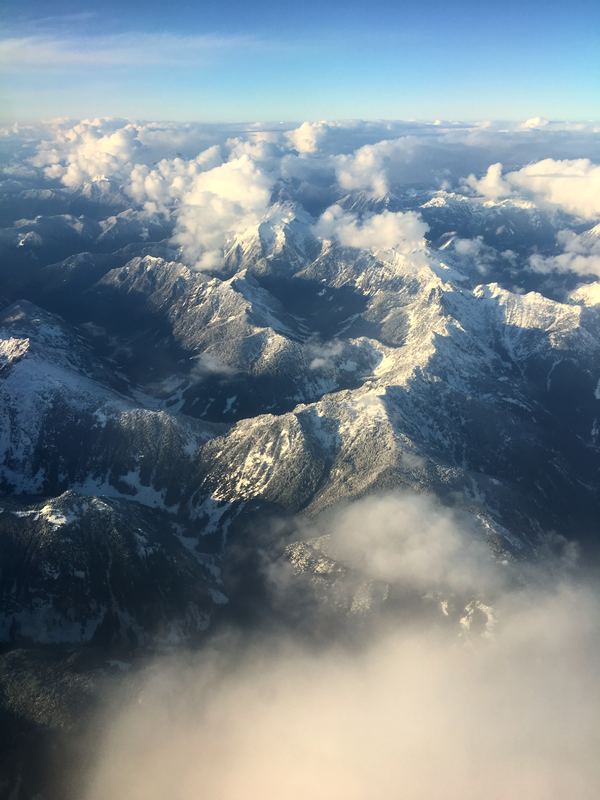 Aerial jagged snow ridges poking through a thick cloud sea.