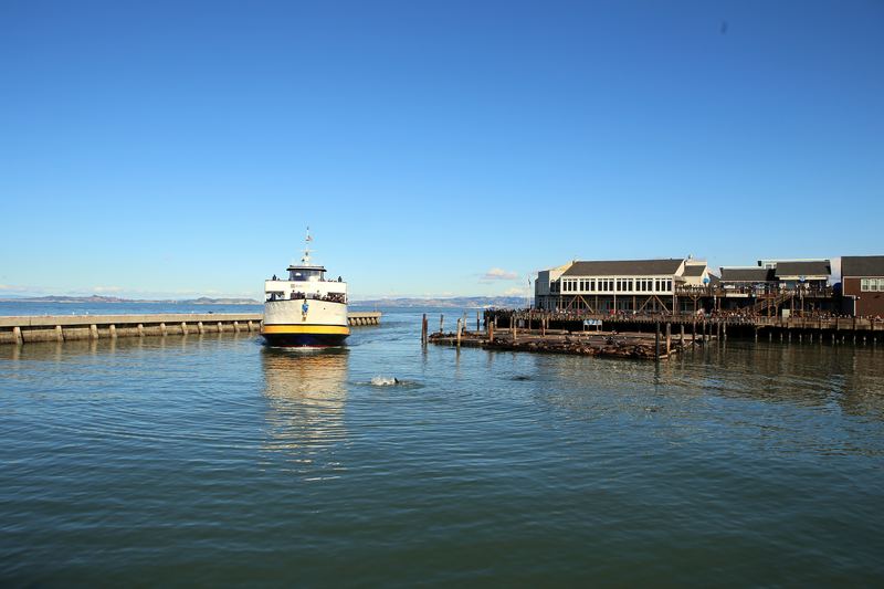 Ferry near a wooden pier with low buildings on blue water.