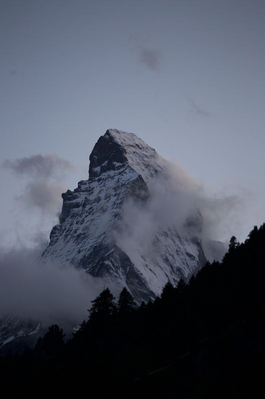 Moody Matterhorn pyramid alone in swirling grey cloud.