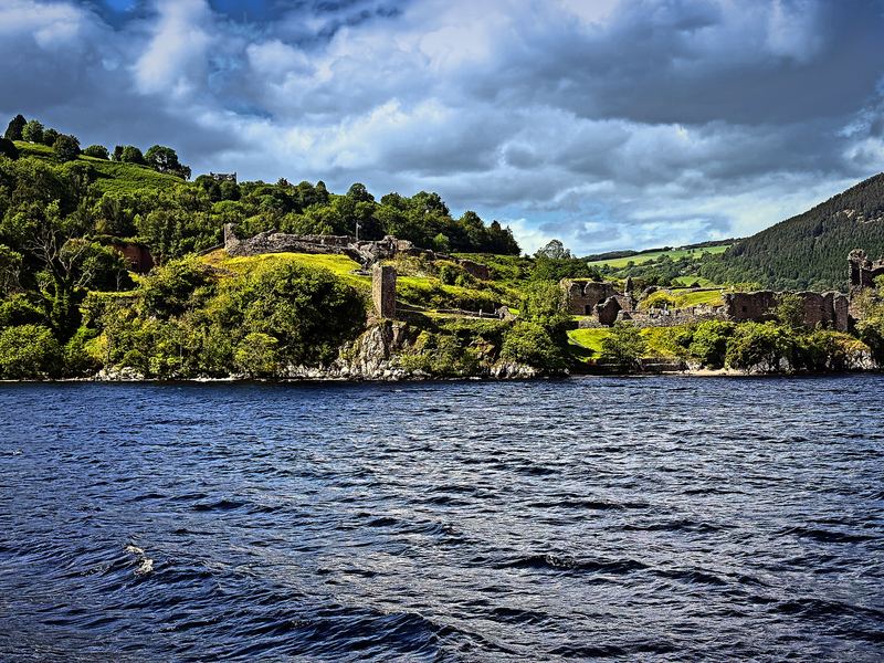 Ruined stone tower on a green hill over dark blue water.